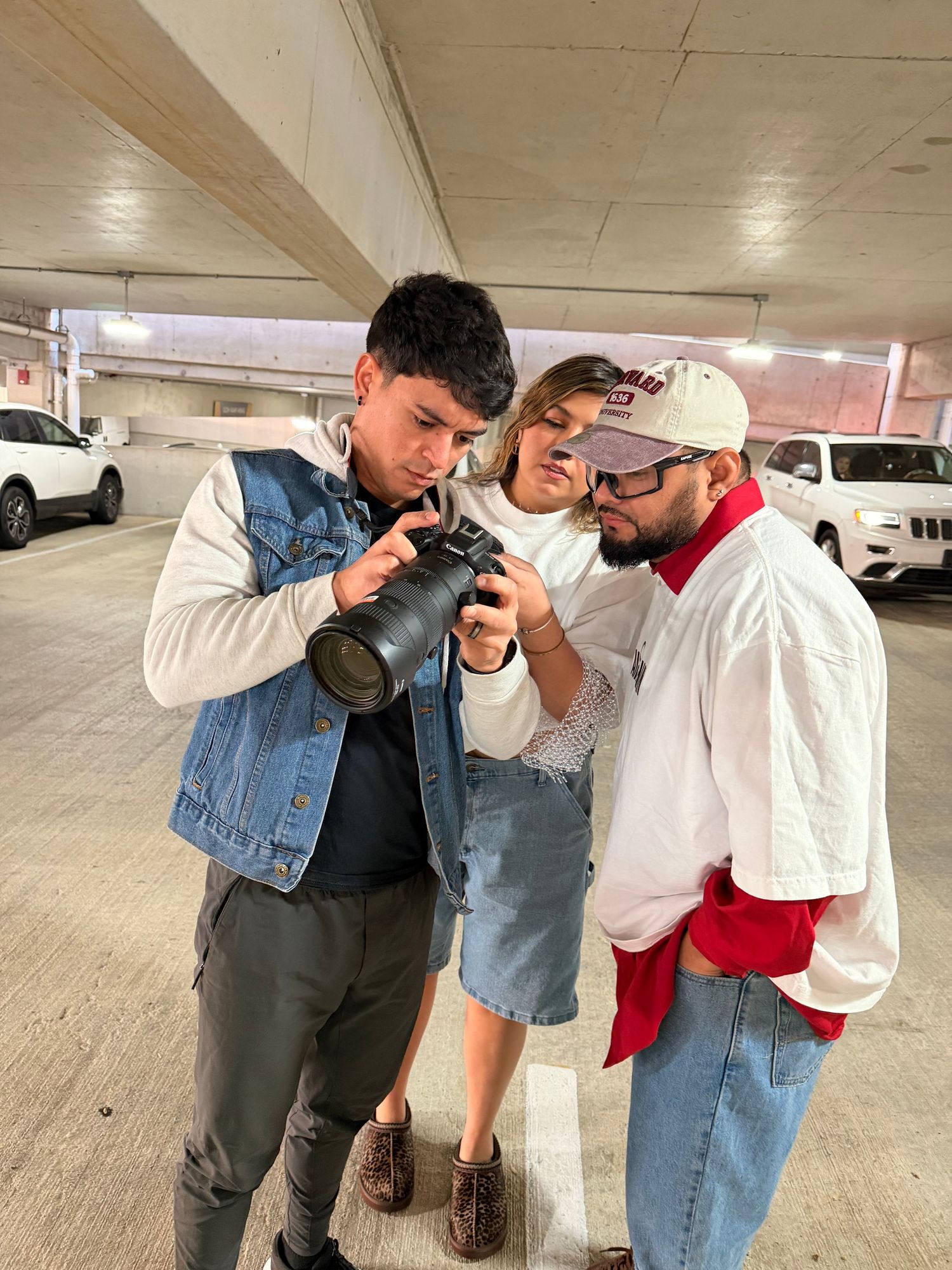 Three people in a parking garage reviewing photos on a camera with a telephoto lens.