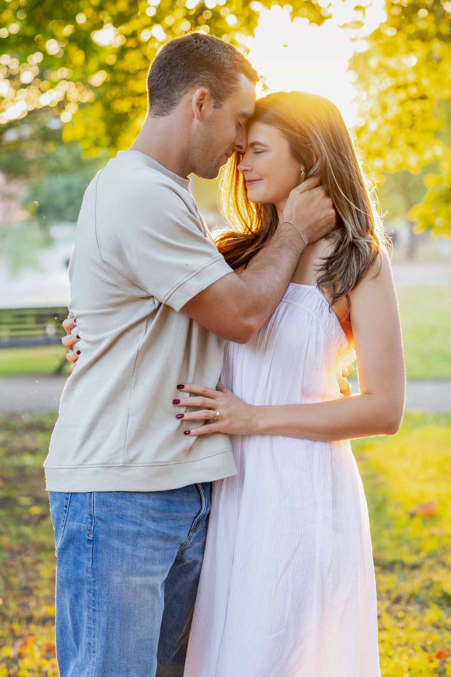 Romantic couple embracing in a sunlit autumn park with golden foliage in the background.