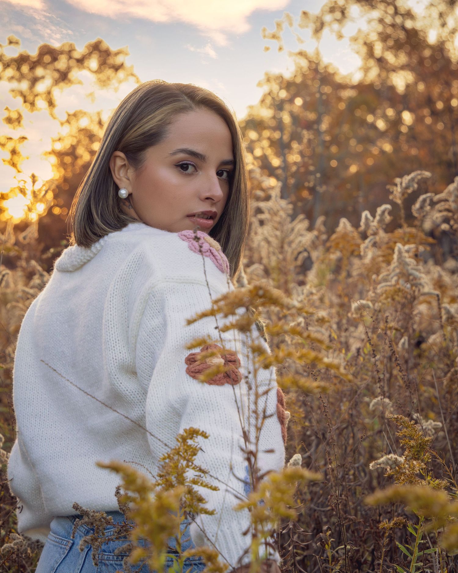 Fall portrait in white turtleneck sweater among golden dried grasses at sunset.