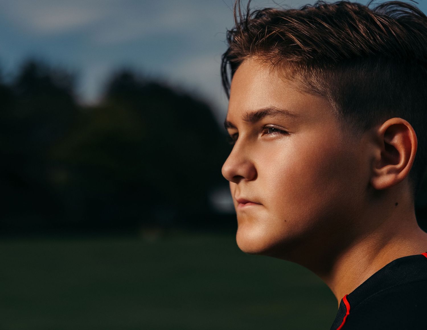 A young teenage boy in profile view gazes thoughtfully into the distance outdoors with soft natural lighting.