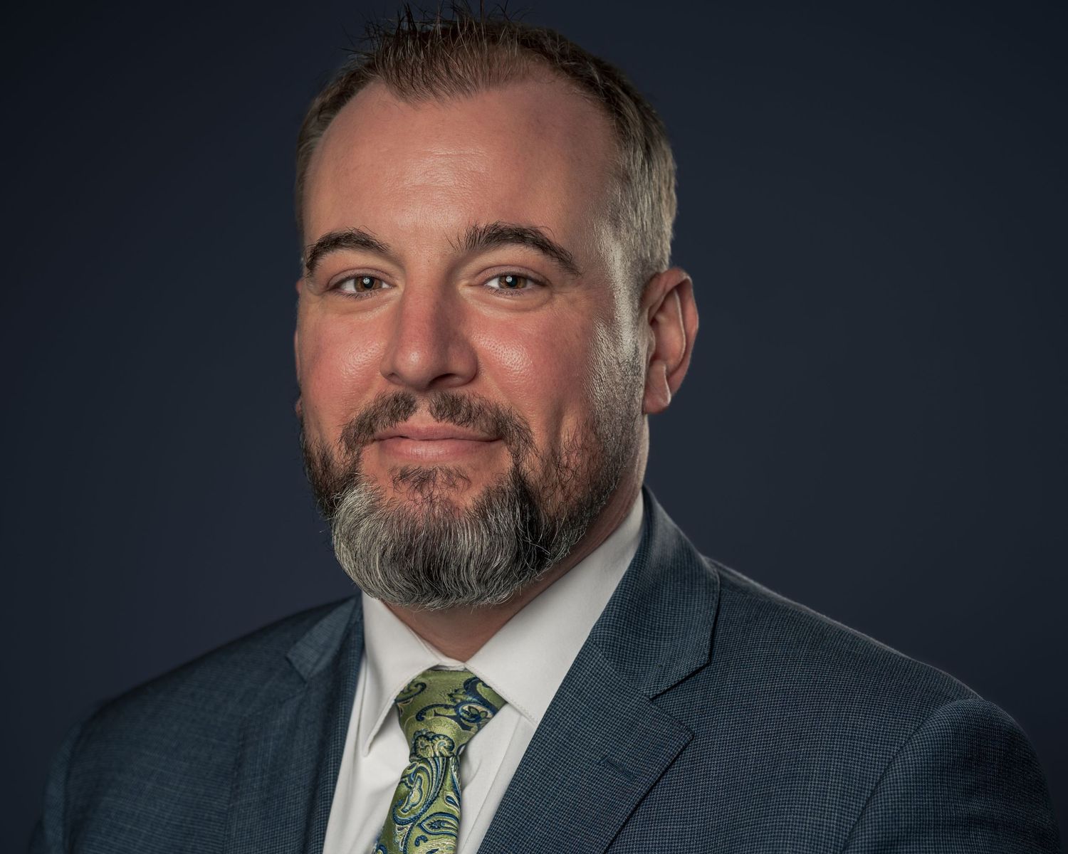 Professional male attorney in gray suit and green tie posing for a formal business headshot.