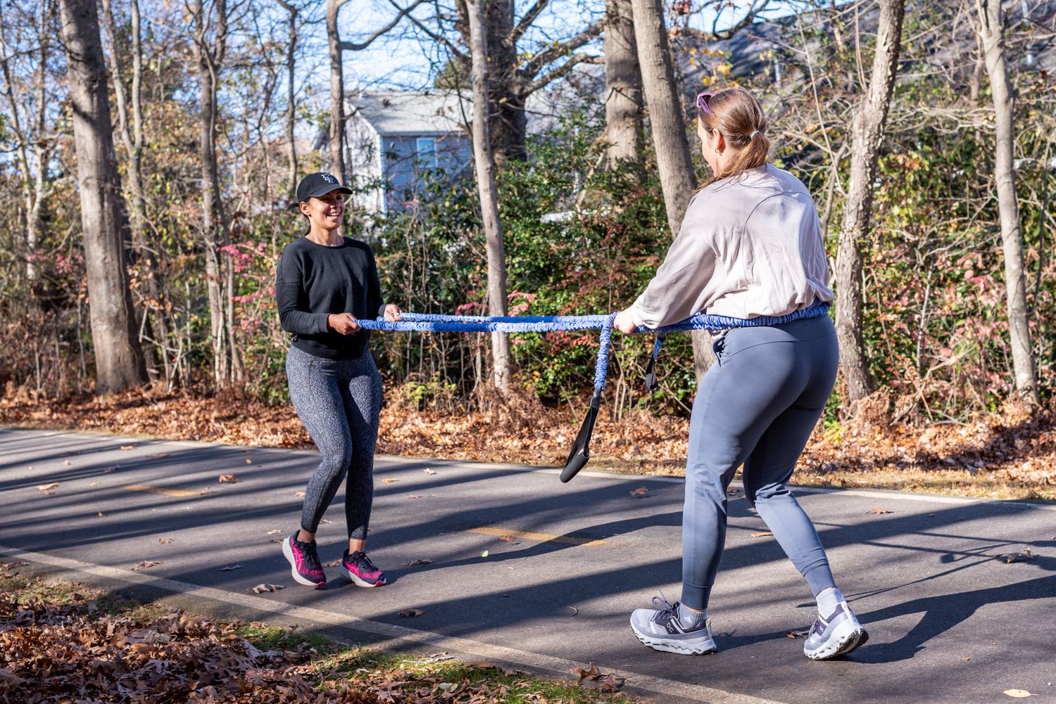 Two women exercising outdoors with resistance bands on a sunny day, surrounded by trees.