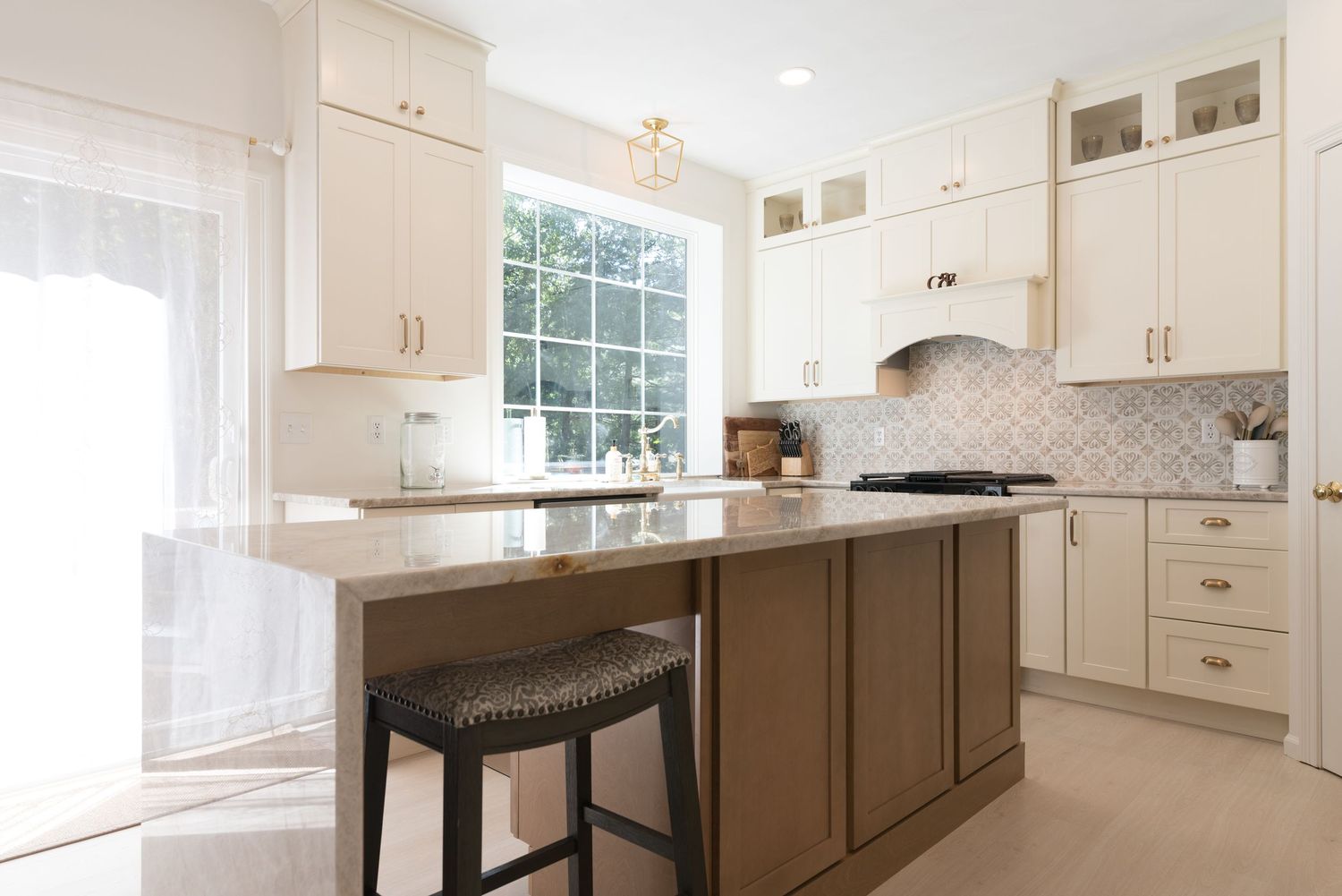 Bright kitchen with white cabinets, marble backsplash, dark wood island, quartz countertops, and bar stool seating.
