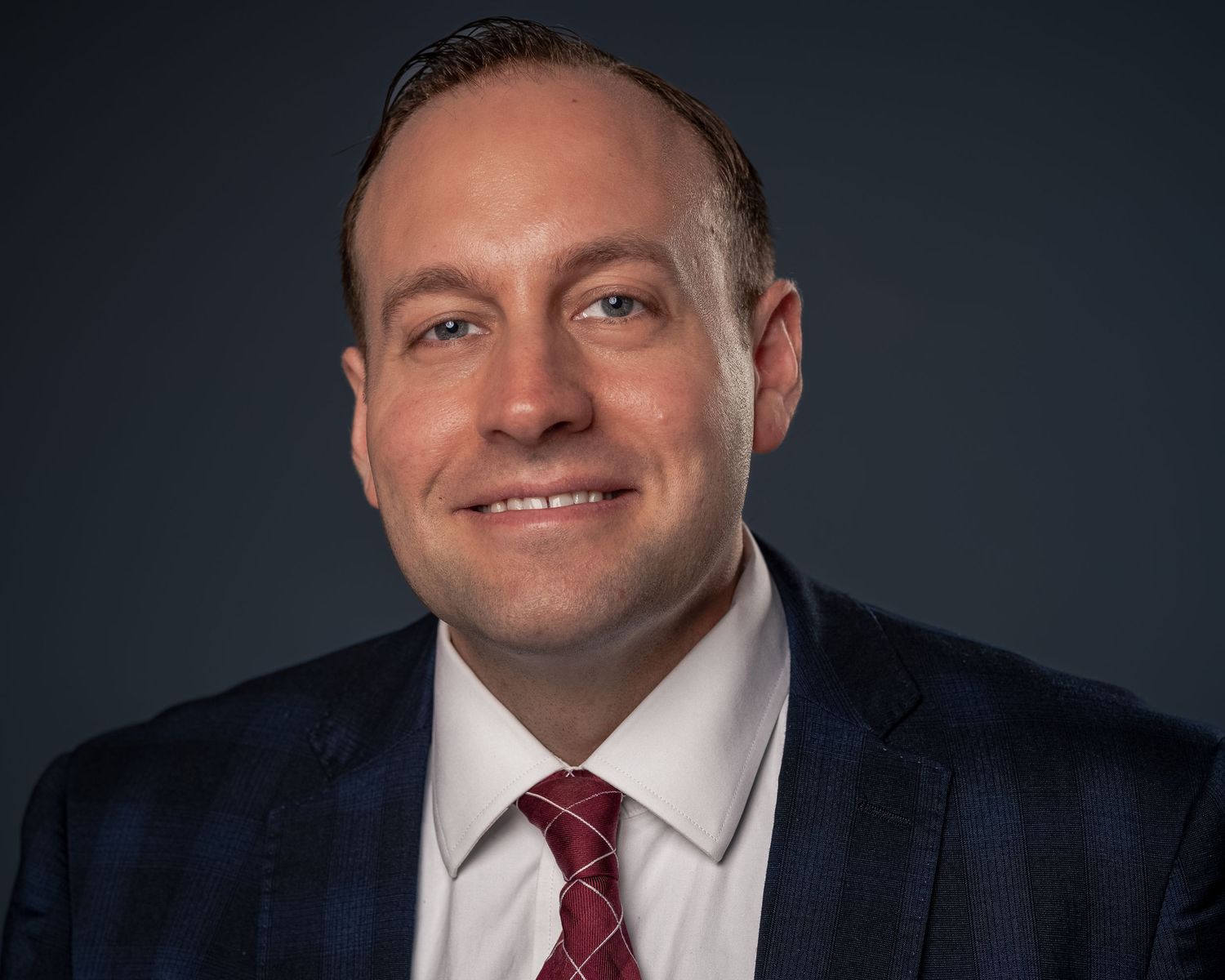 Professional man in navy suit and red tie smiling for a corporate business headshot portrait.