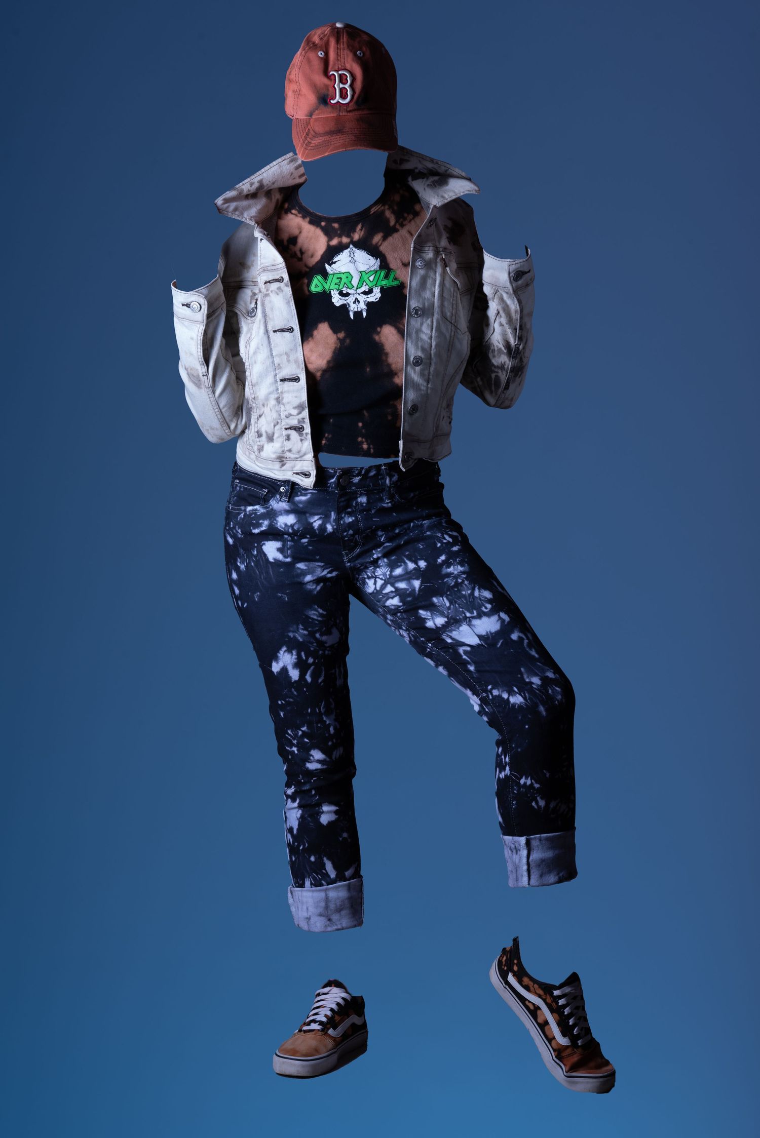Floating headless mannequin wearing tie-dye jeans, denim jacket, graphic tee, and red baseball cap.