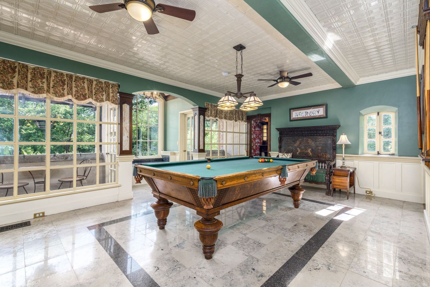 Elegant billiard room with marble floors, teal walls, coffered ceiling, and large windows flooding natural light.