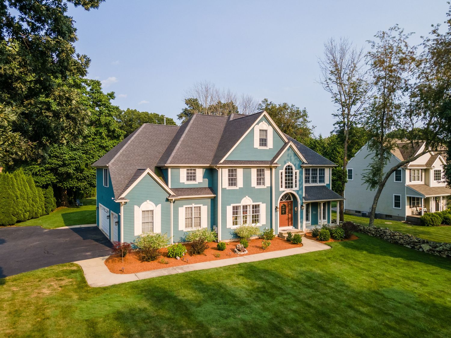 Stunning blue colonial home with manicured lawn and attached garage surrounded by mature trees.