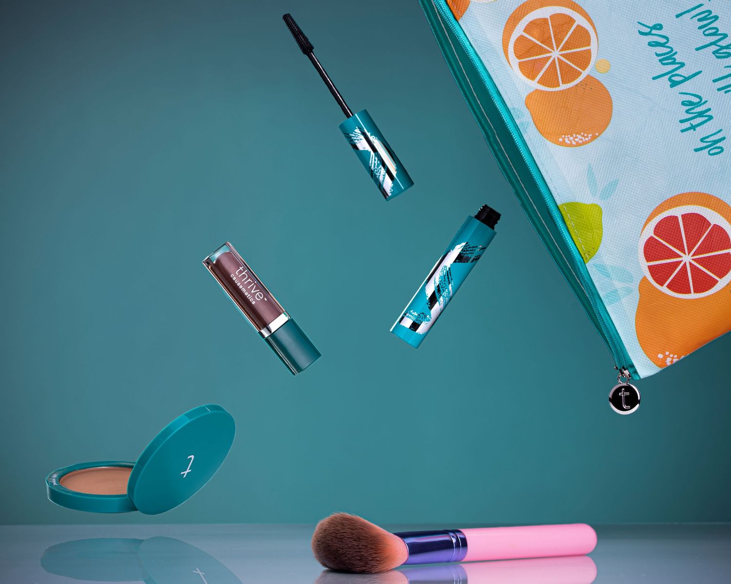 Floating makeup products including mascara, lip gloss, powder compact, and brush spilling from a teal cosmetic bag.