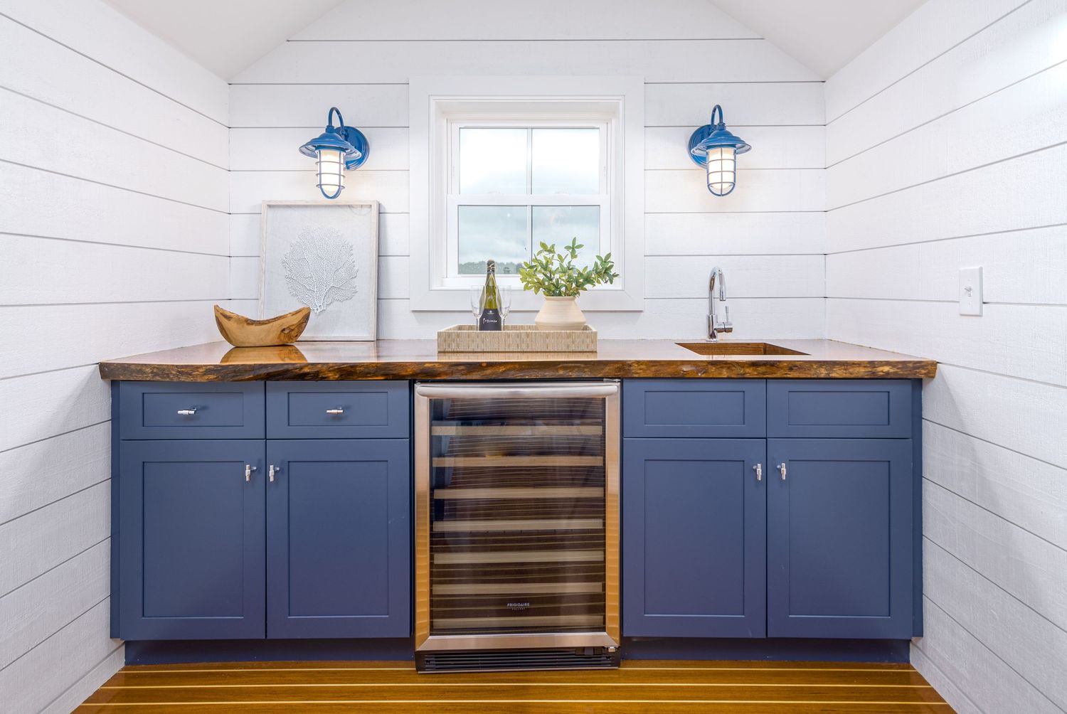 Navy blue kitchen cabinets with butcher block countertop and wine fridge under vaulted shiplap ceiling.