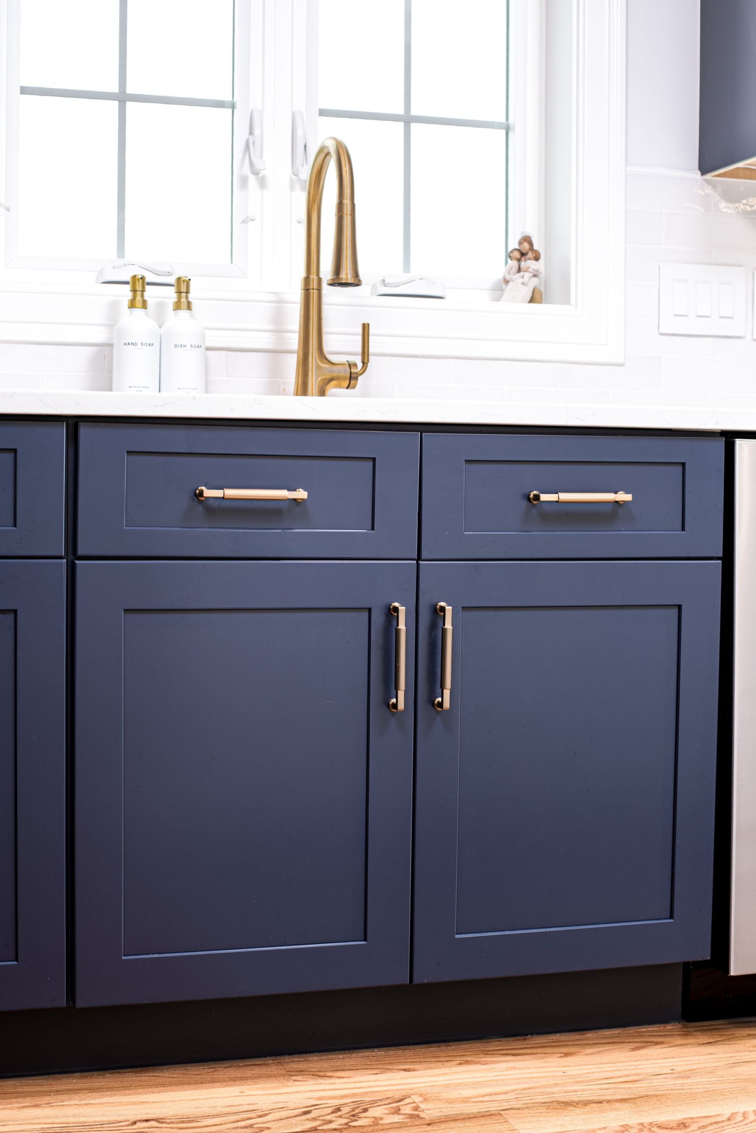 Navy blue shaker-style kitchen cabinets with gold brass hardware and faucet.