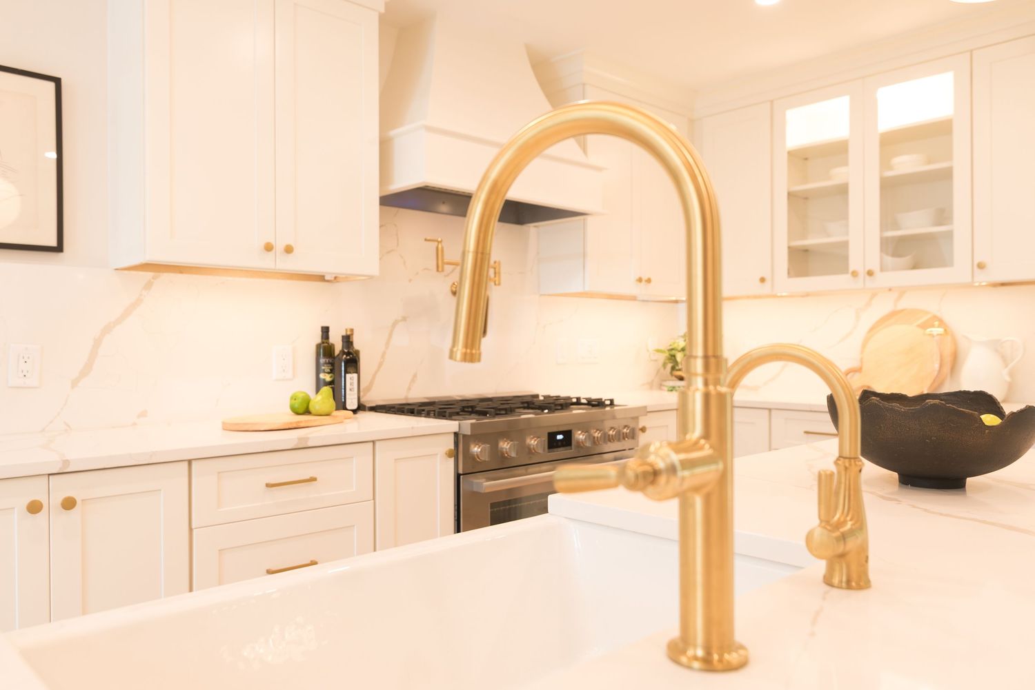 White kitchen with gold faucet, marble countertops, white cabinets, and stainless steel range.