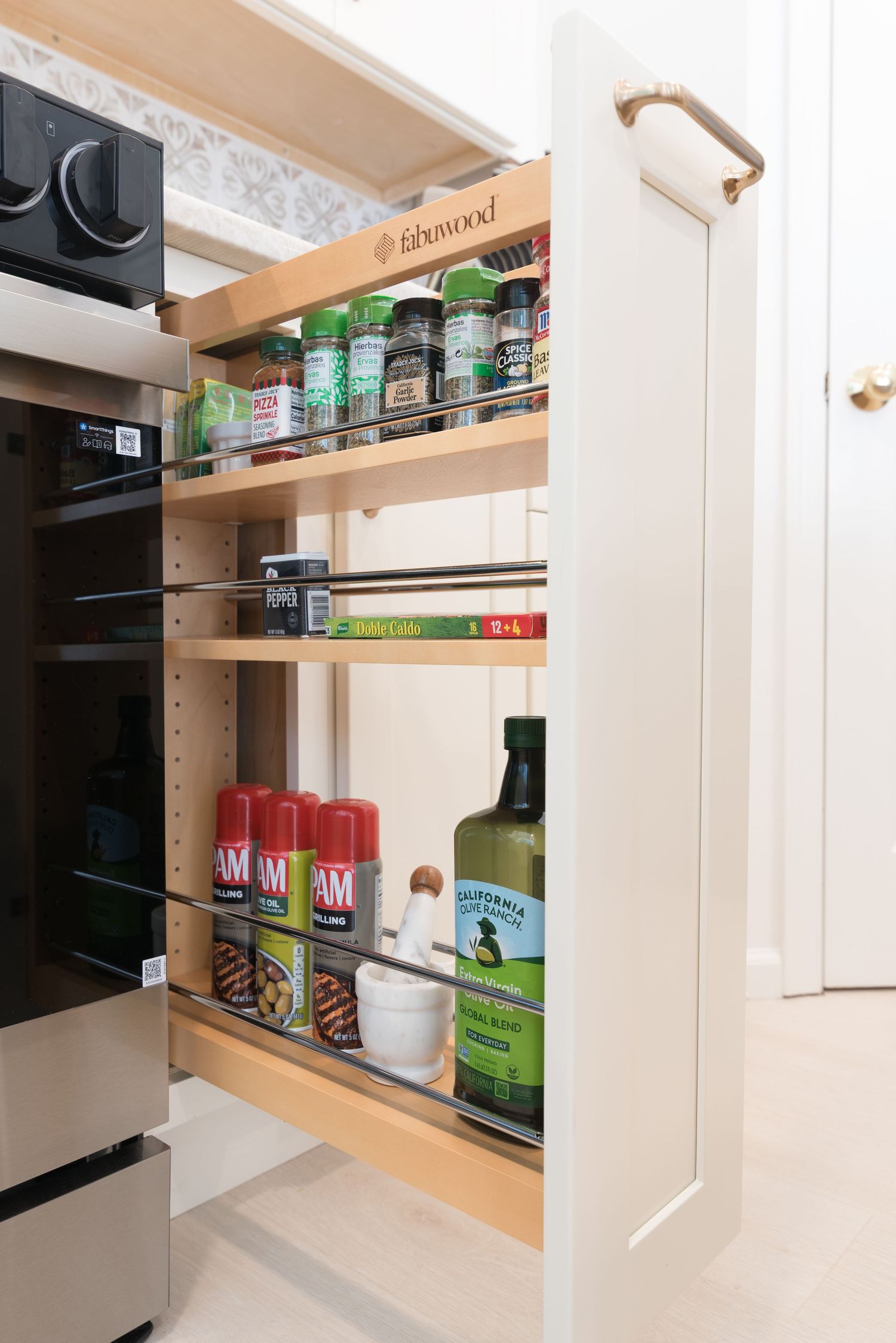 Pull-out spice rack cabinet organizer with wooden shelves storing spices, cooking sprays, and olive oil in a modern kitchen.