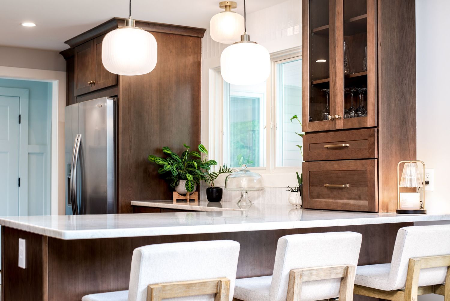Modern kitchen with dark wood cabinets, white quartz island, globe pendant lights, and bar stools.