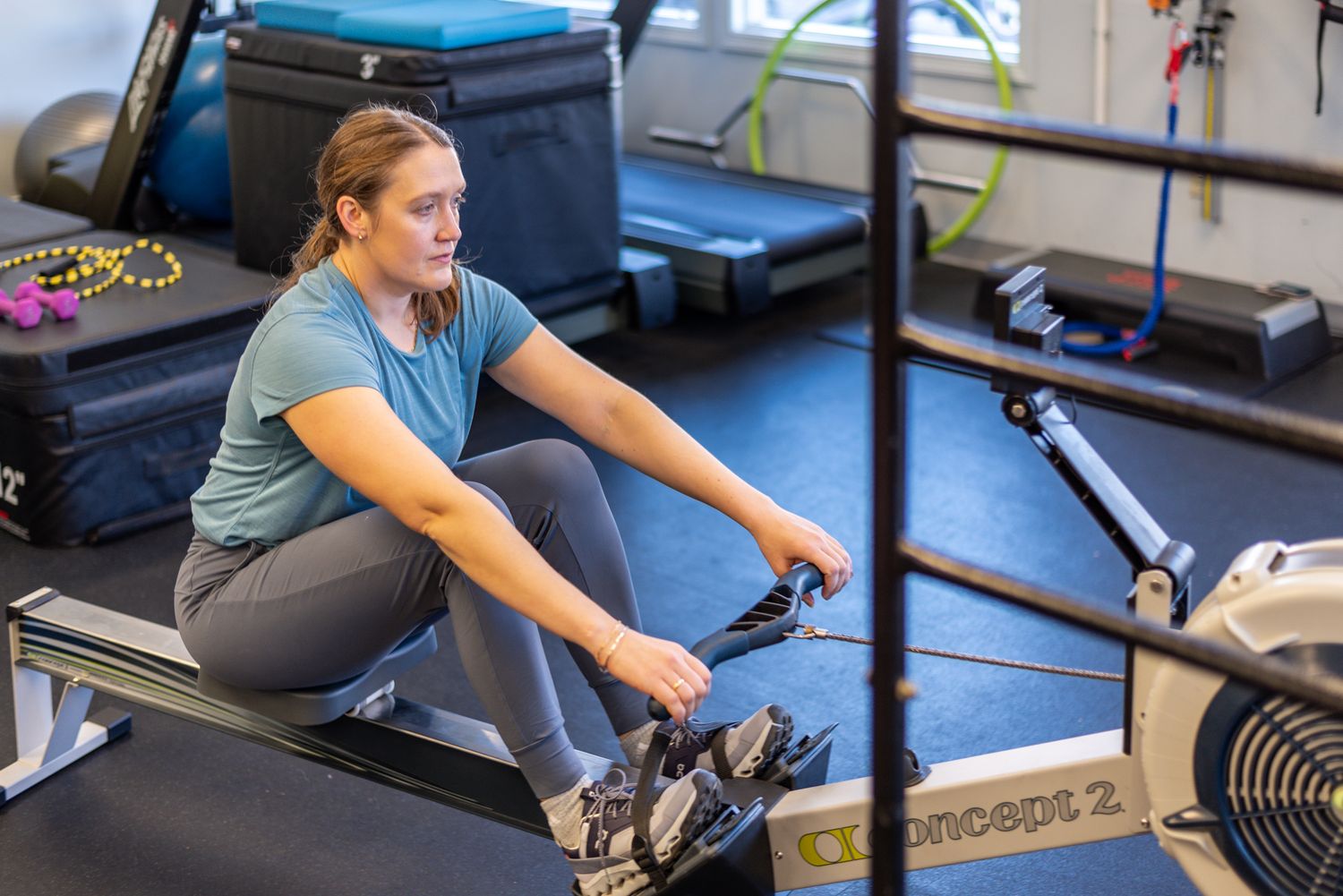 Woman exercising on a Concept2 rowing machine in a modern gym during an indoor fitness workout session.