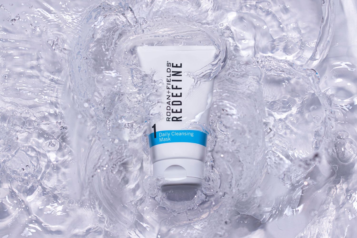 Rodan and Fields Redefine Daily Cleansing Mask tube laying on a wet surface with water ripples.