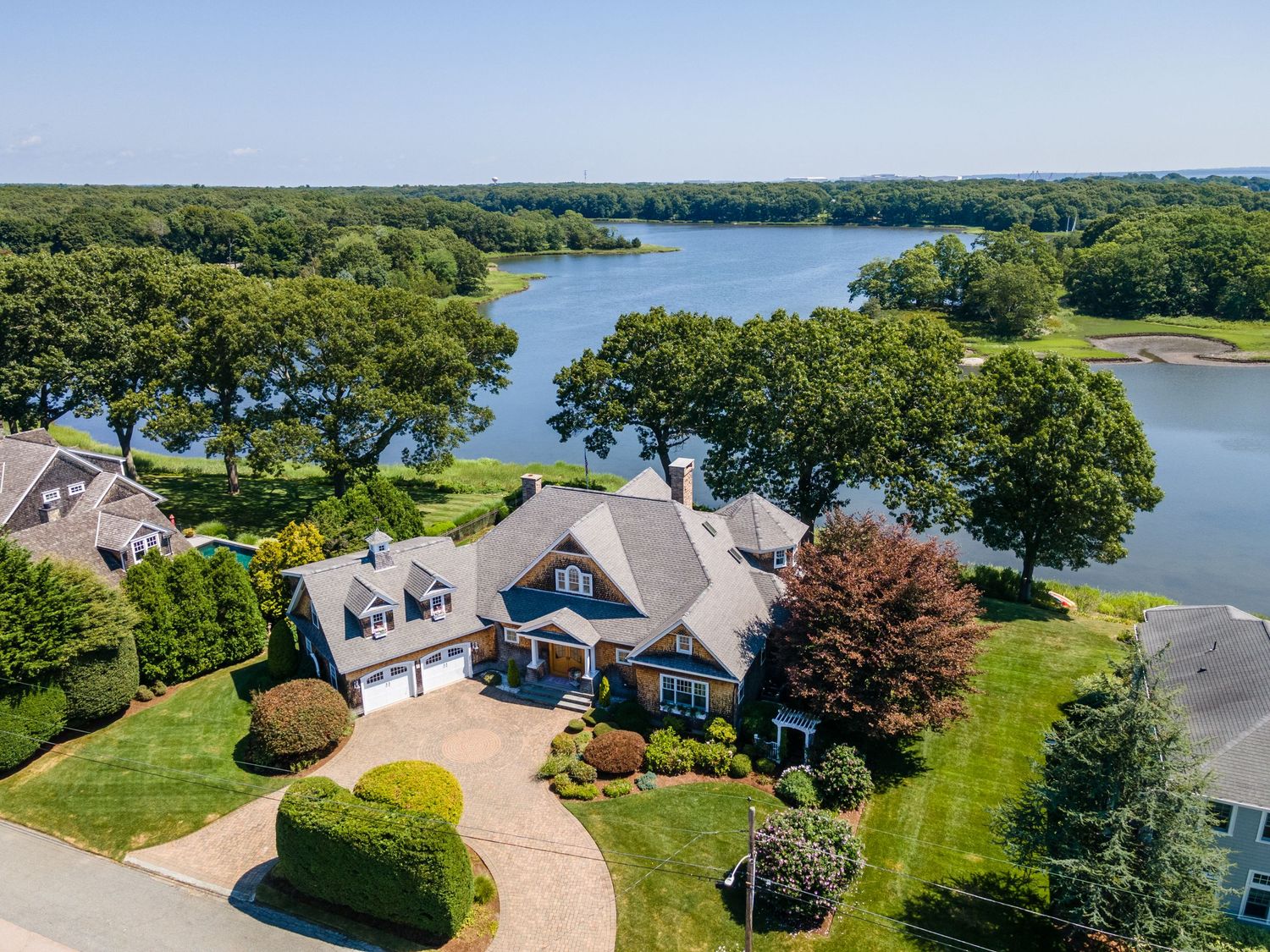 Aerial view of luxury lakefront home with circular driveway surrounded by serene water views.