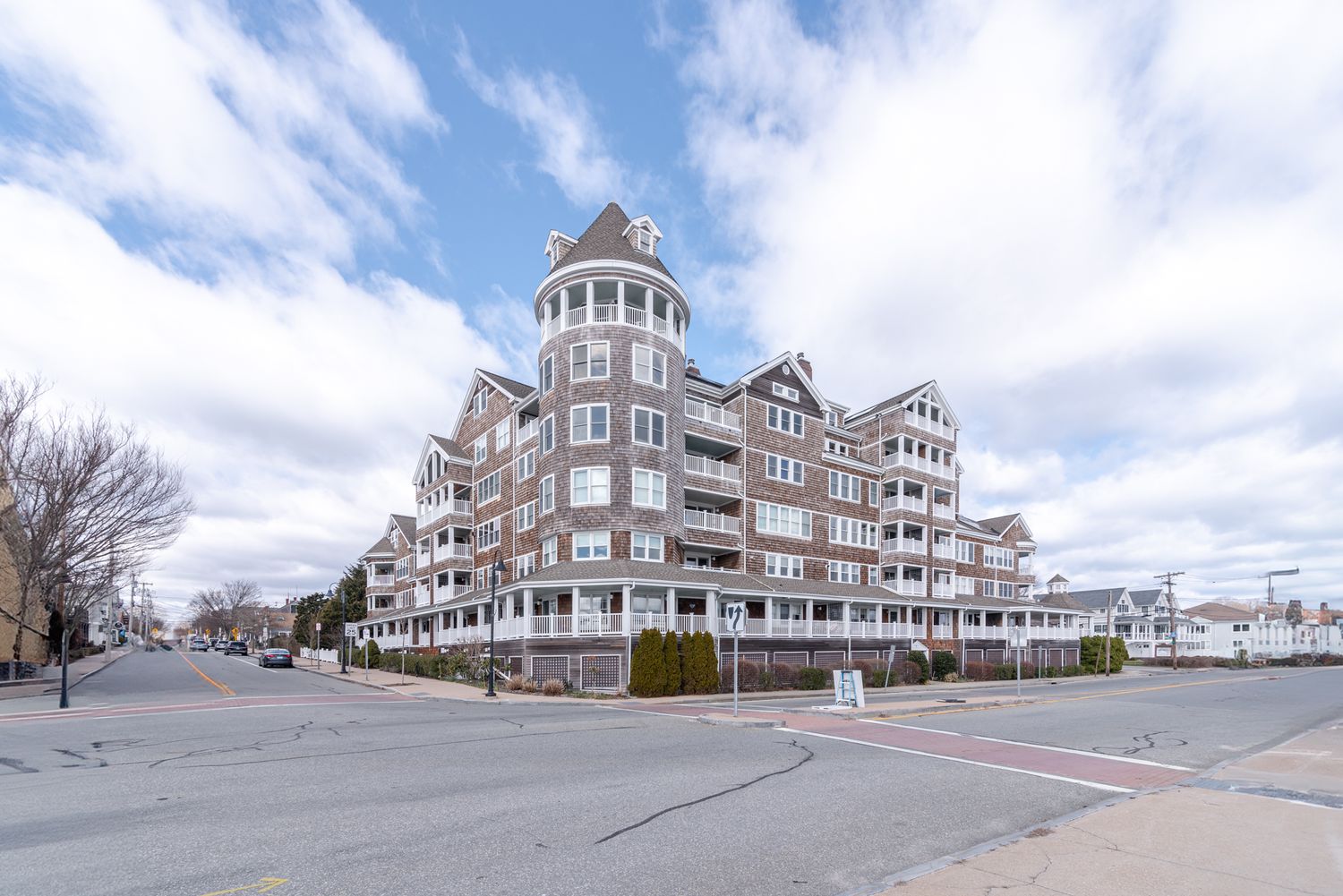 Large brick waterfront condominium building with tower turret under partly cloudy skies.