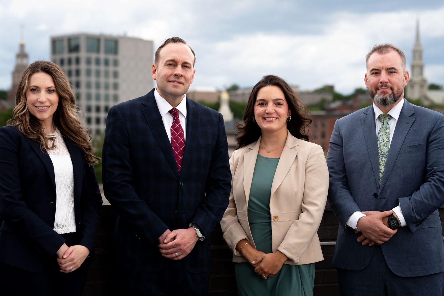 Four legal professionals posing together on a rooftop with Providence Rhode Island skyline in background.