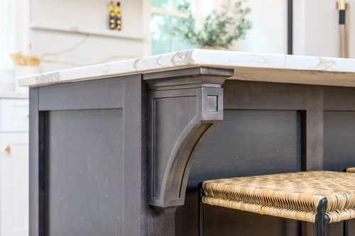 Close-up of gray kitchen island corbel detail with marble countertop and wicker stool.