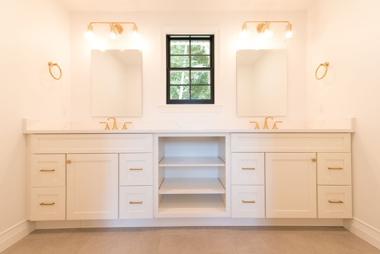 White double vanity with gold hardware, open shelving, dual mirrors, and a black window in a bright bathroom.