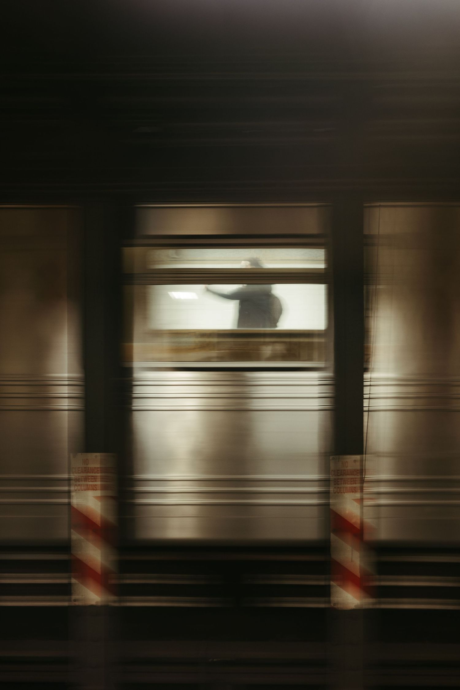 Blurry motion shot of a train door window with metallic columns and hazard stripes in a dark subway station.