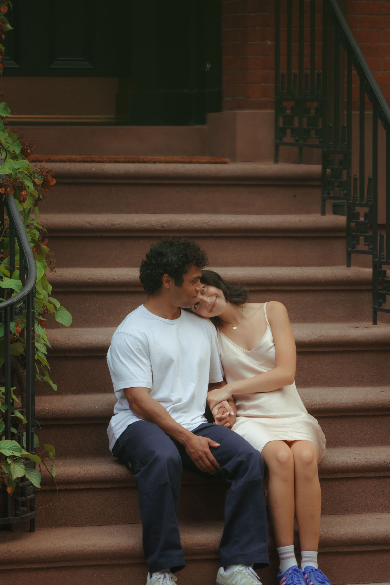 A couple sits close together on brownstone steps in a romantic moment.