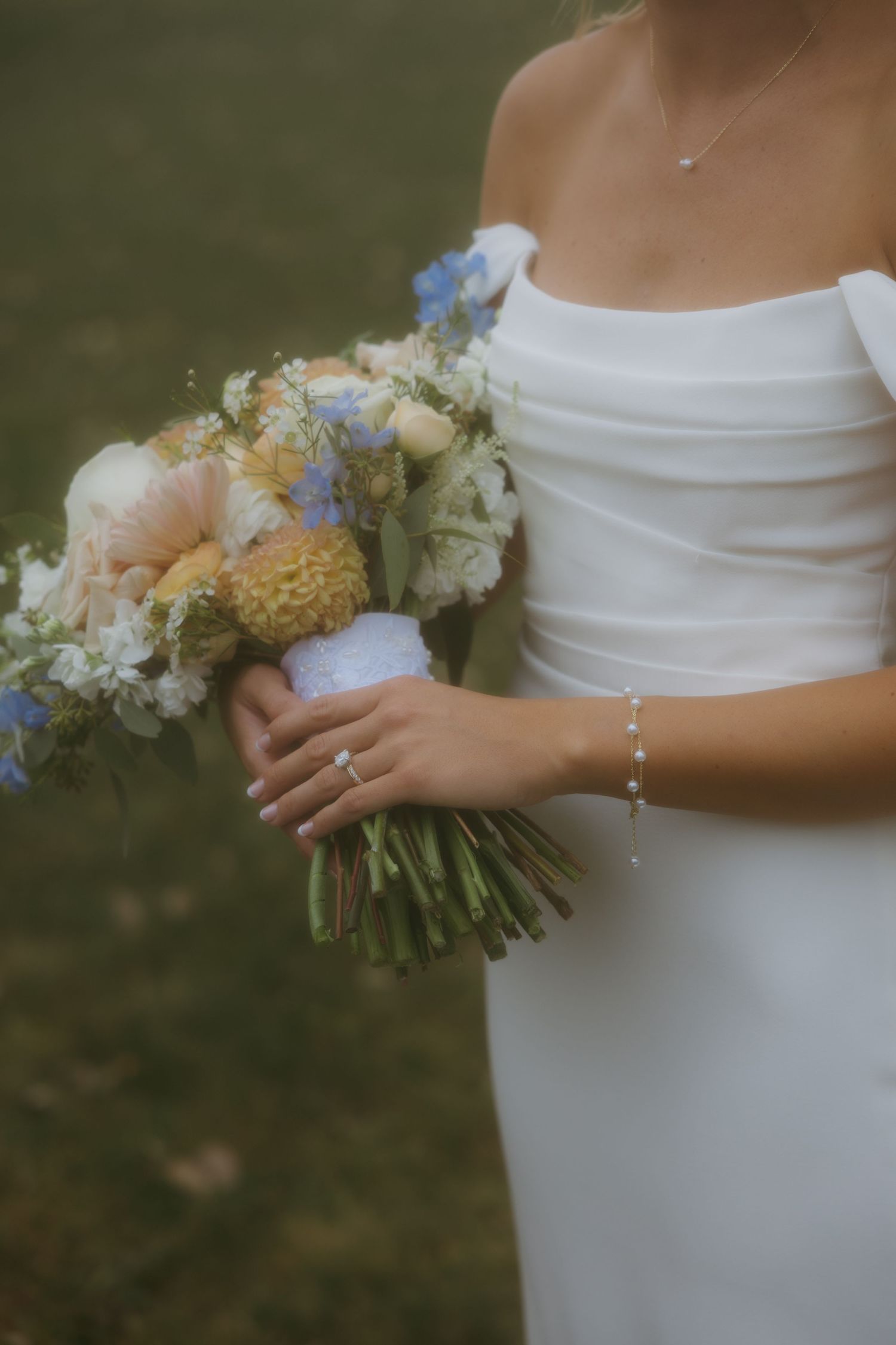 A delicate bridal bouquet with peach, white and blue flowers held against a simple white wedding dress.