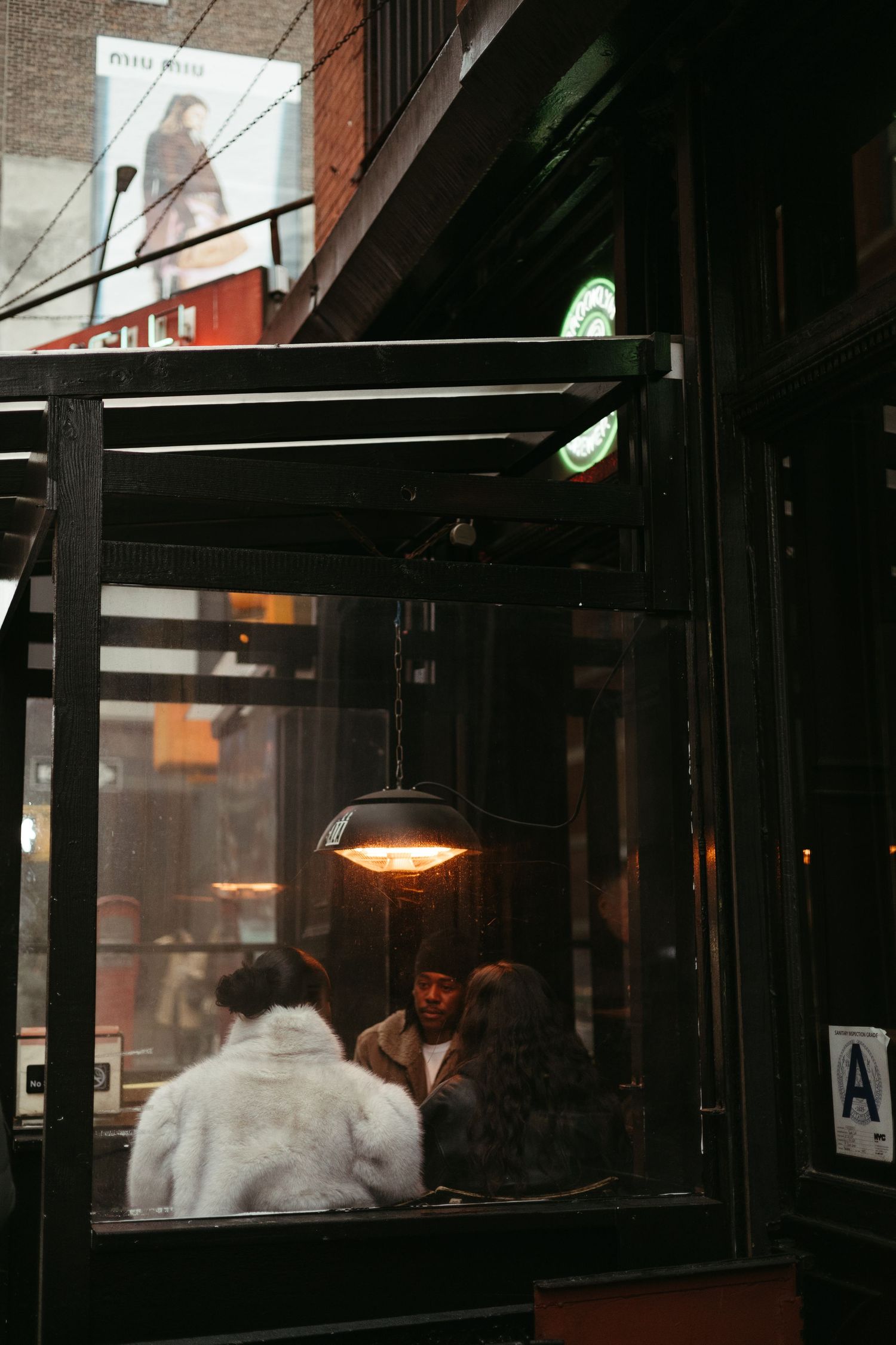 People dining inside a cozy restaurant at night with warm lighting and glass windows creating an intimate atmosphere.