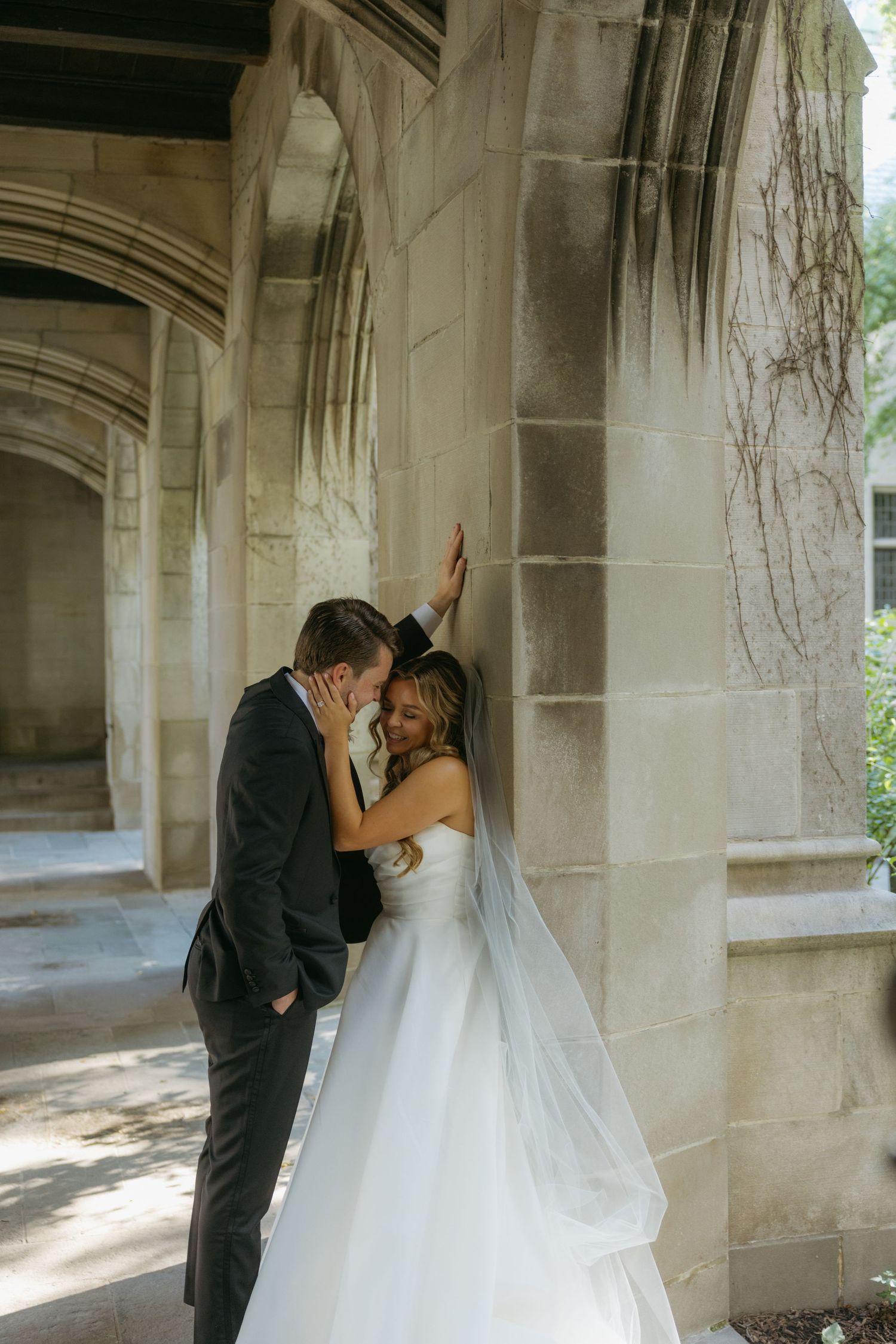 A romantic wedding moment captured under stone archways with dramatic lighting and shadows.