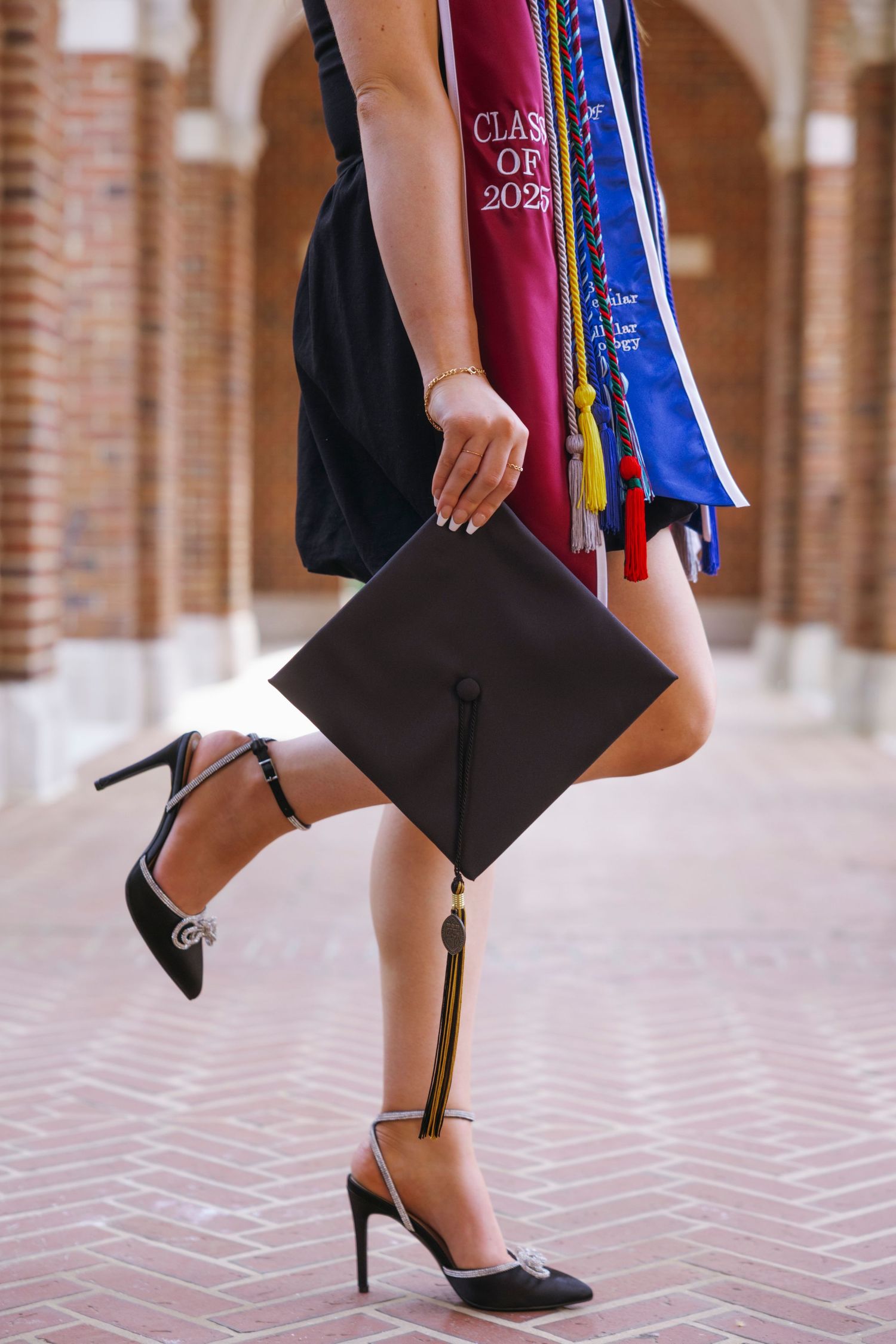 Graduate in high heels holds mortarboard cap while wearing graduation sash and stole with Class of 2023 regalia.