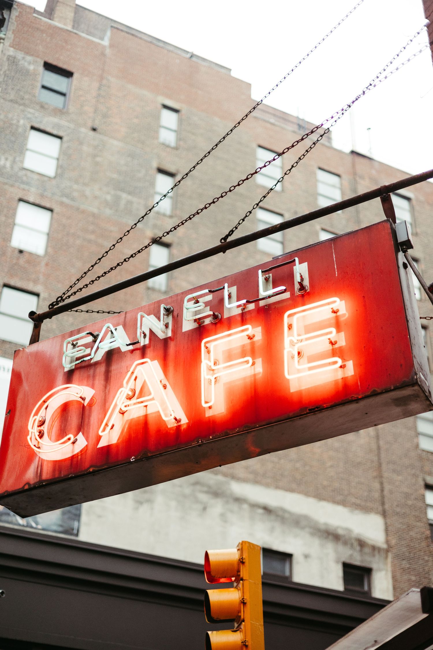A vintage neon sign for a cafe glows red against a brick building facade in an urban setting.