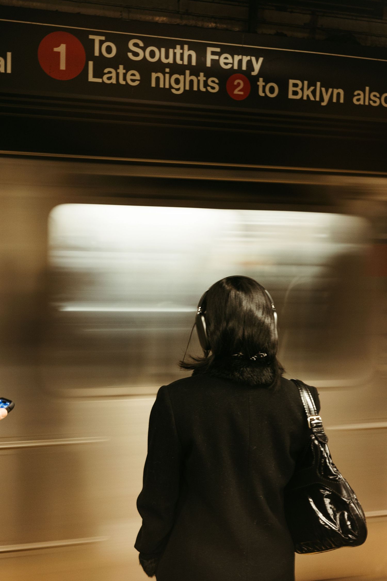A person wearing black waits for a train to South Ferry on a subway platform in New York City.