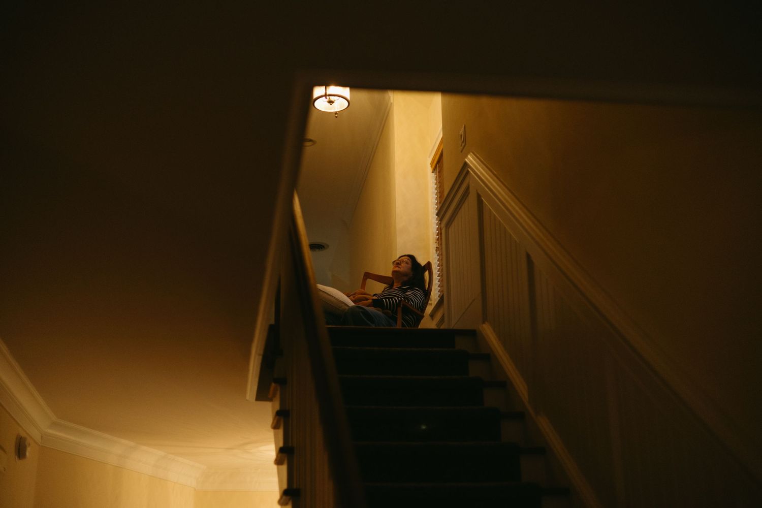 A dark and moody stairwell illuminated by warm overhead lighting casting dramatic shadows on the steps.