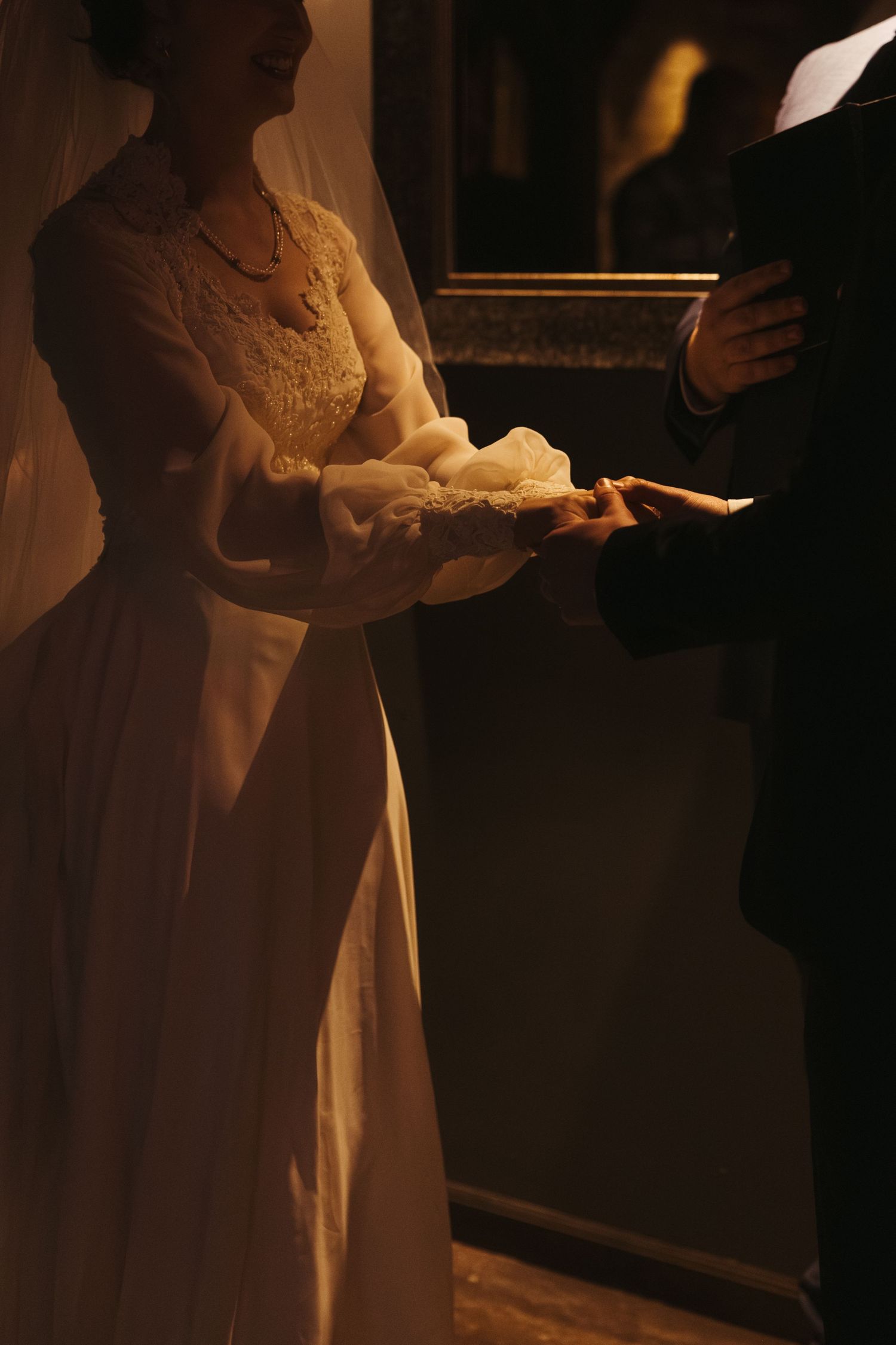 A couple in wedding attire stands close together in a dimly lit room with warm lighting creating a romantic atmosphere.
