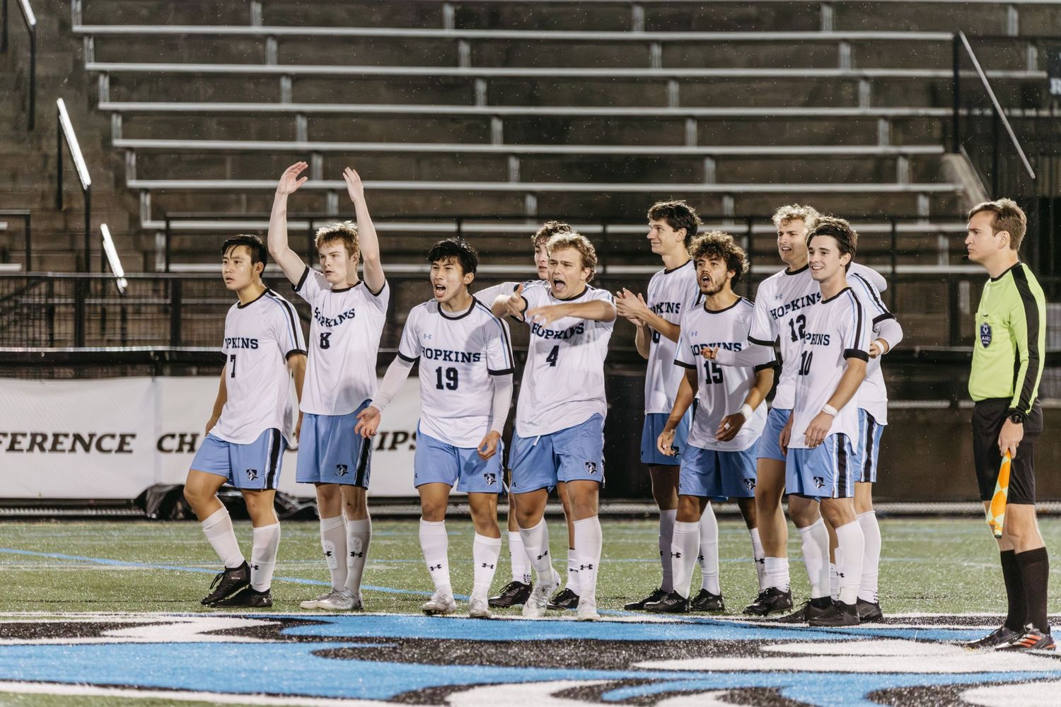 Soccer team lined up on field with players raising their arms in celebration.