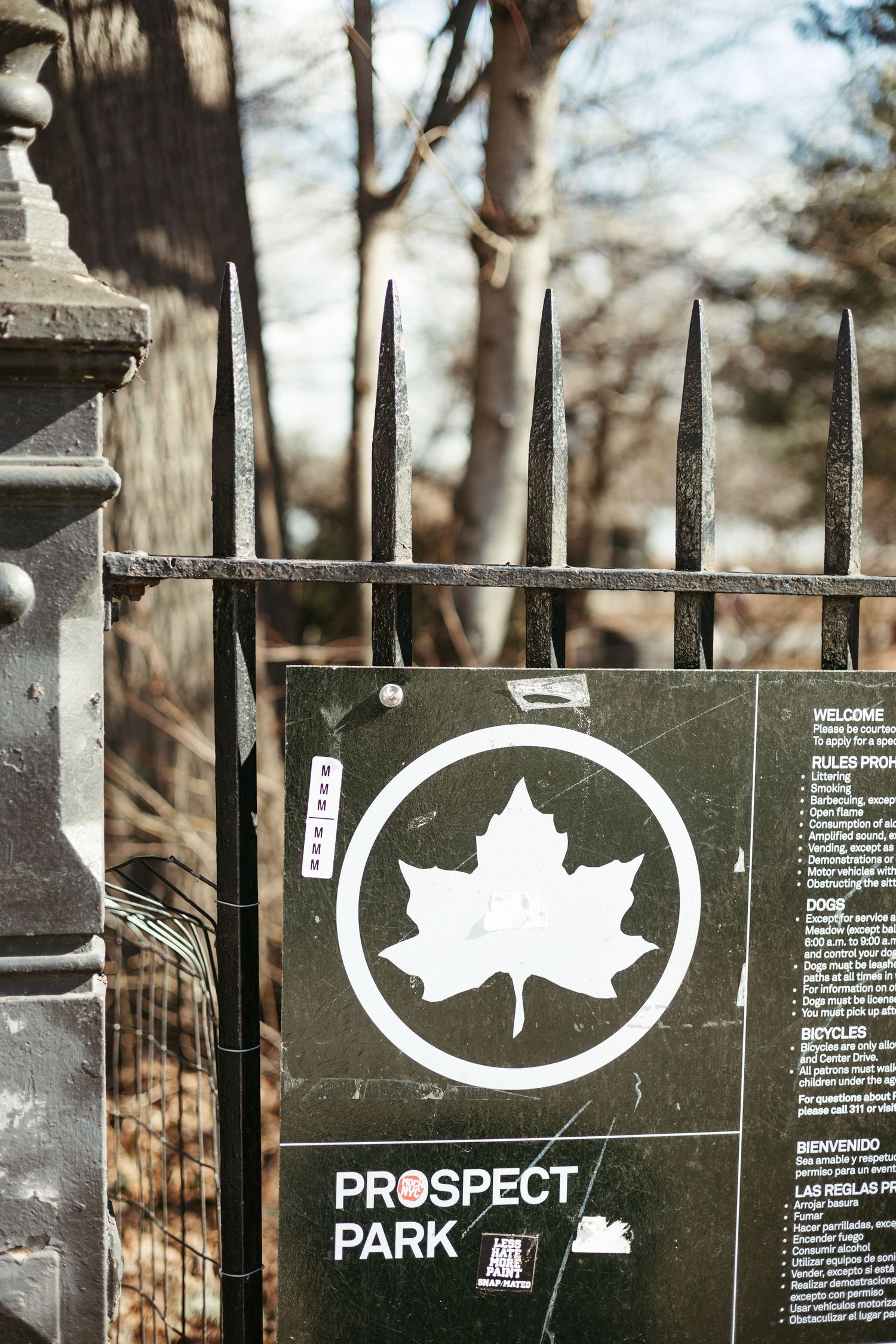 A black and white Prospect Park sign with maple leaf logo mounted on an iron fence in Brooklyn.