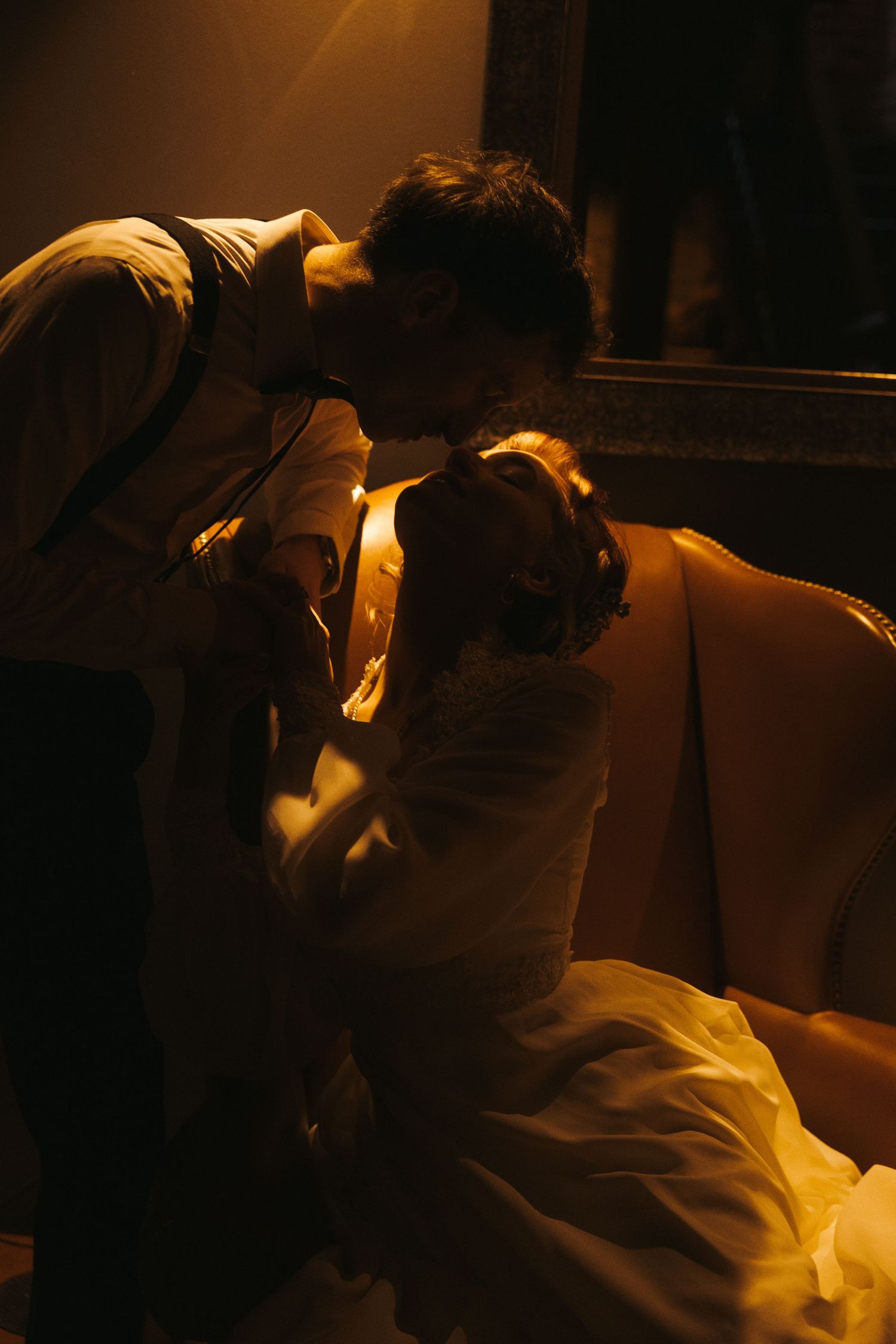 A dramatic moody scene captured in warm golden lighting shows two figures in an intimate moment on a couch.