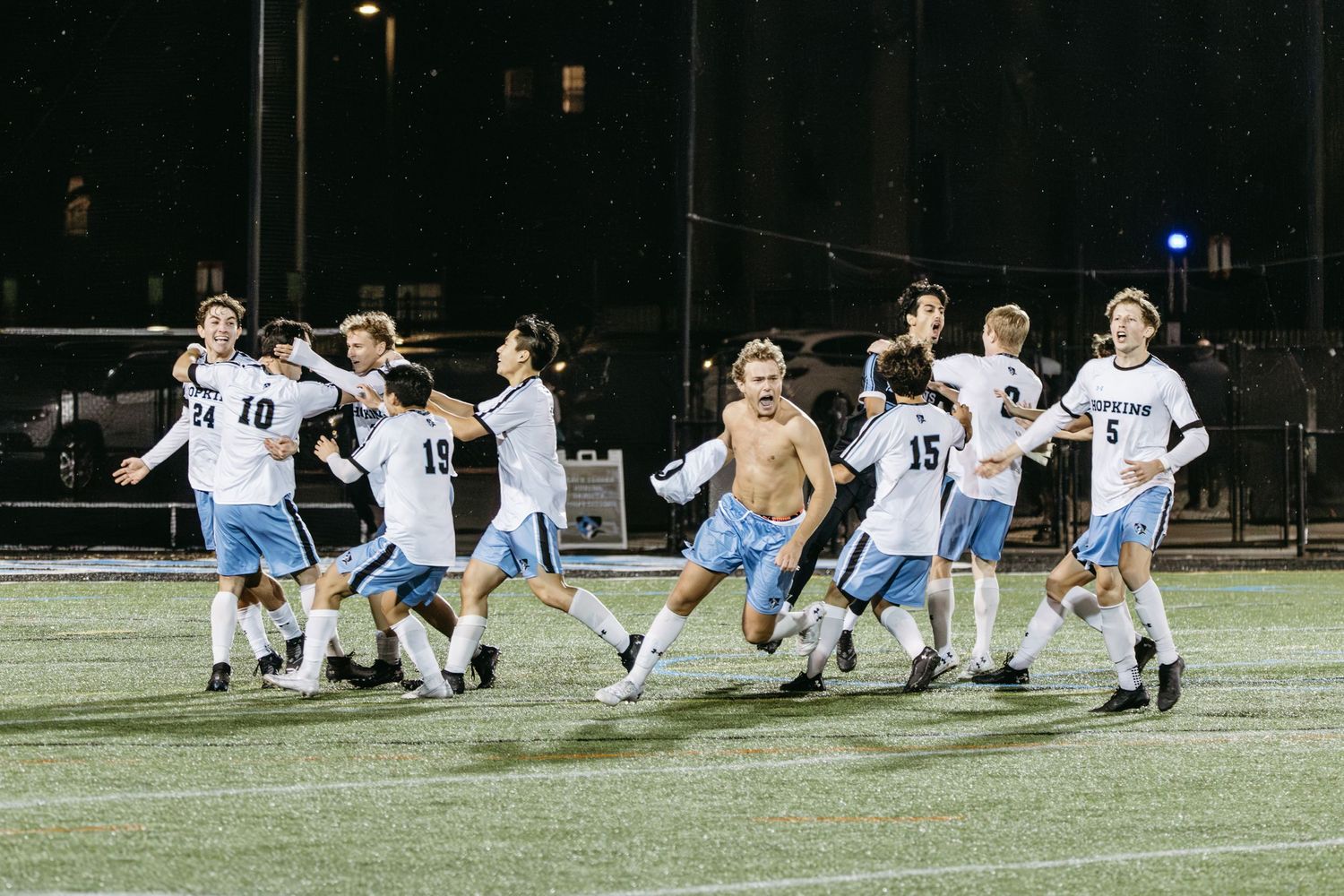 Soccer team celebrates victory by running together on field at night under stadium lights.