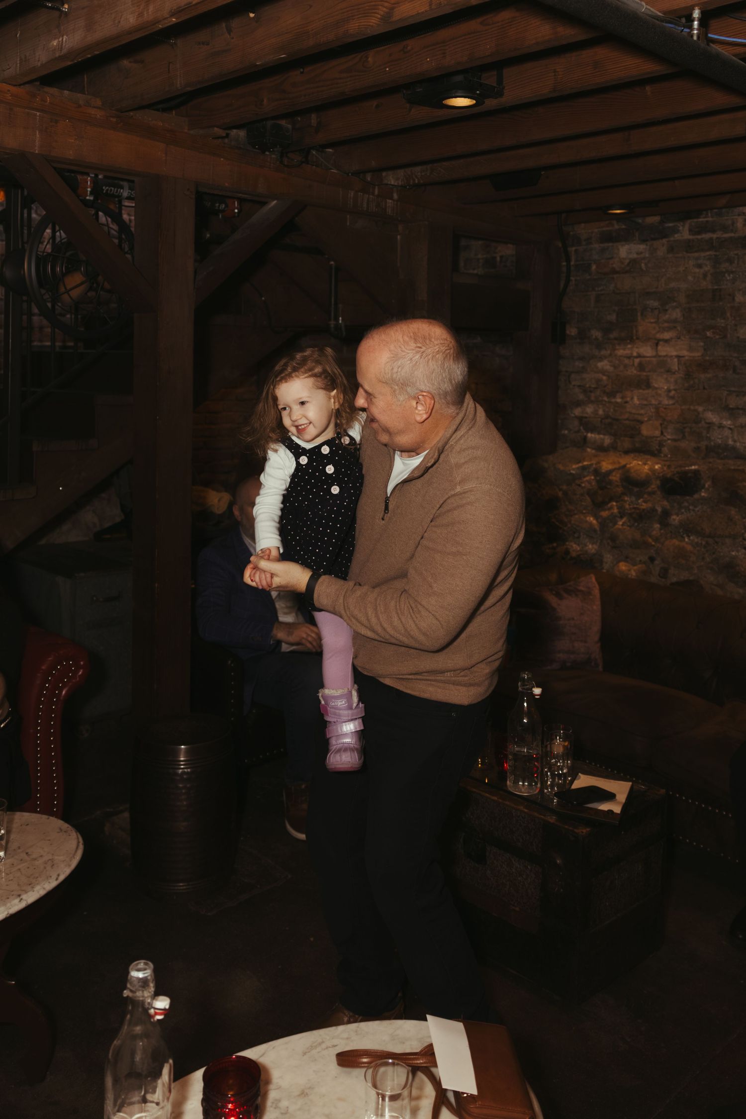 People dancing together in a dimly lit rustic venue with exposed brick walls and wooden beams.