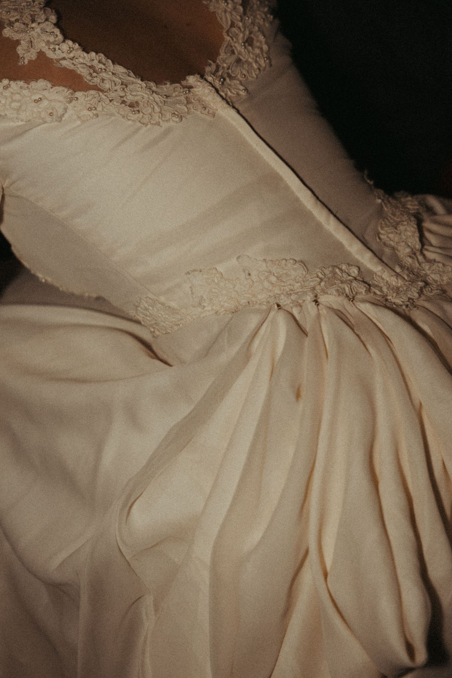 Close-up details of delicate lace trim and pleated fabric on a vintage-style cream colored dress or gown.