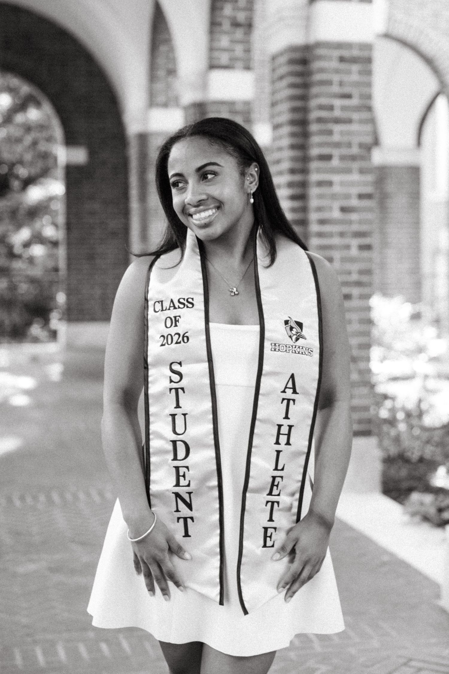 Black and white photo of a smiling college student athlete wearing a Class of 2026 Student Athlete sash outdoors.