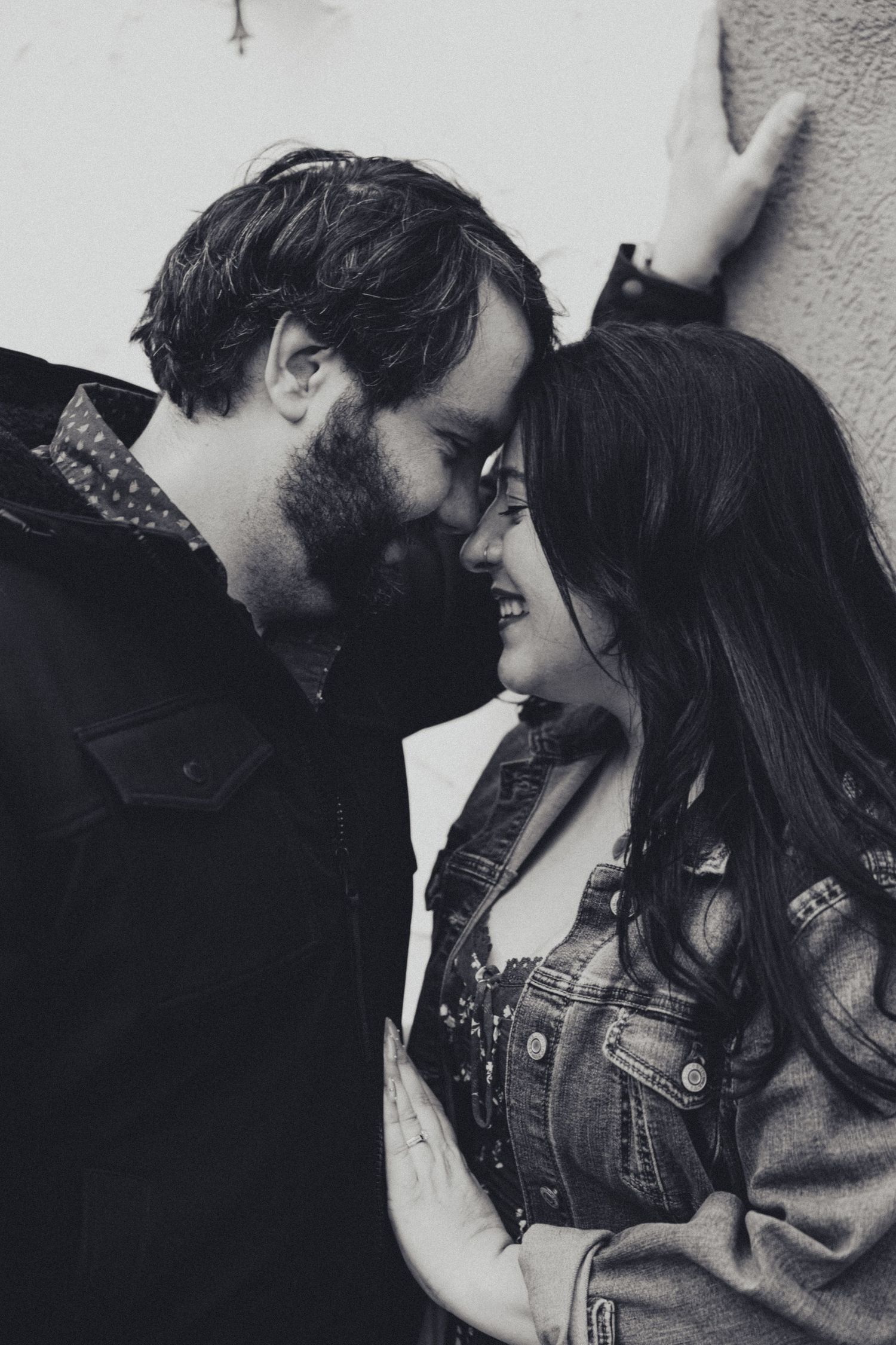 A romantic black and white portrait of a couple sharing an intimate moment against a white wall.
