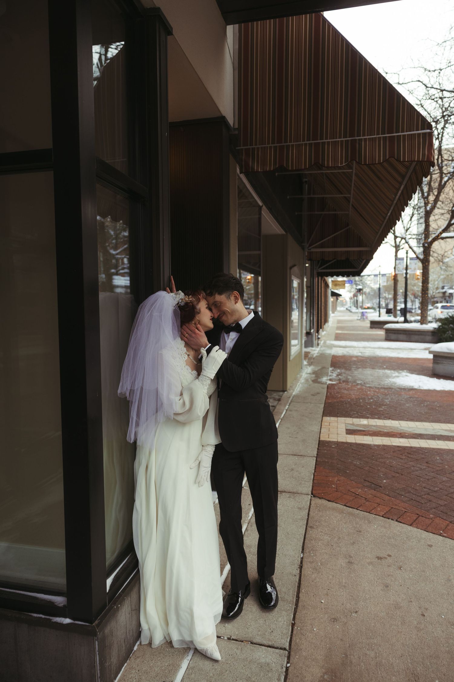 A bride and groom share an intimate moment under an architectural overhang on a brick sidewalk.