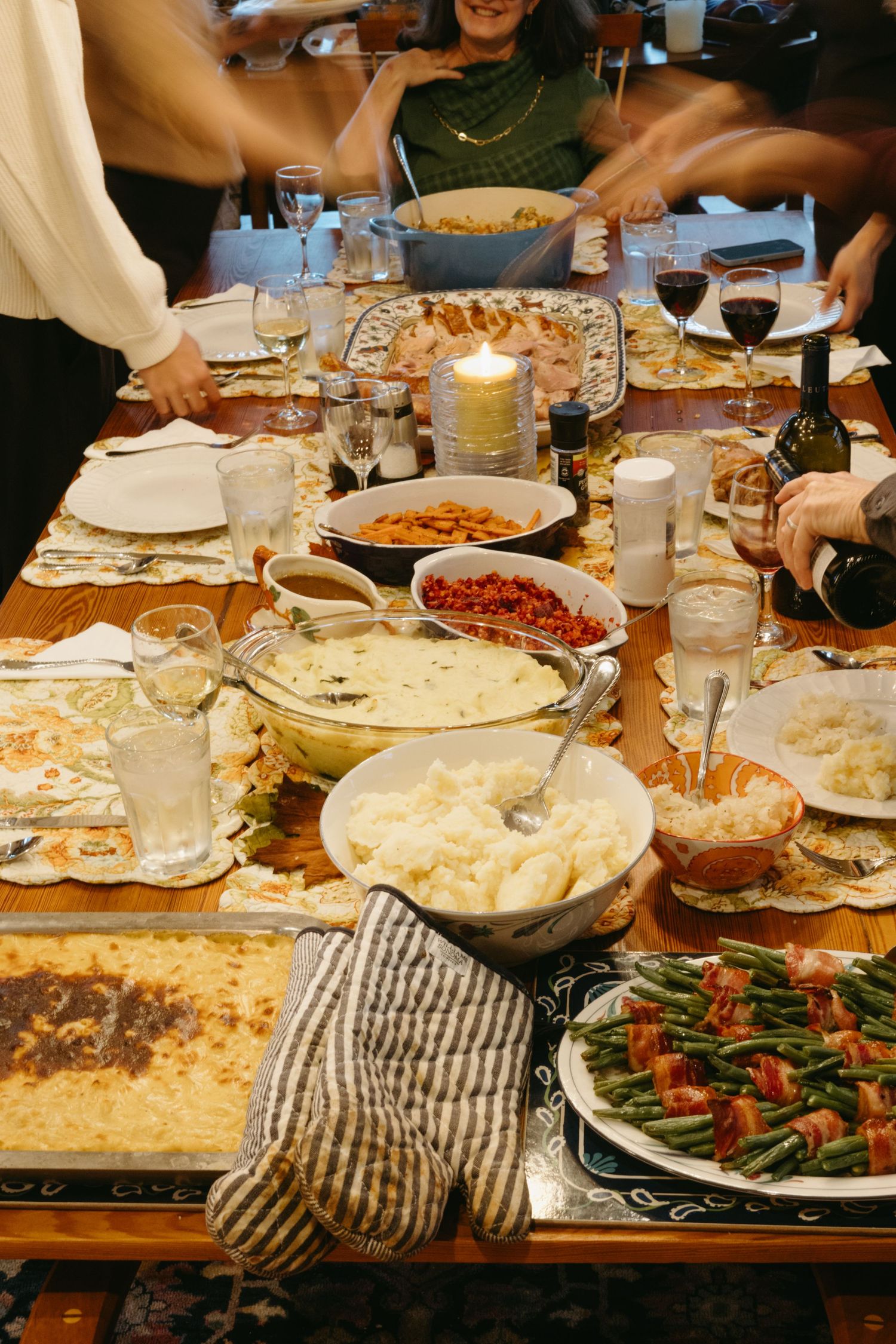 A candlelit dinner table filled with various dishes including green beans, casseroles, and wine glasses for a holiday feast.