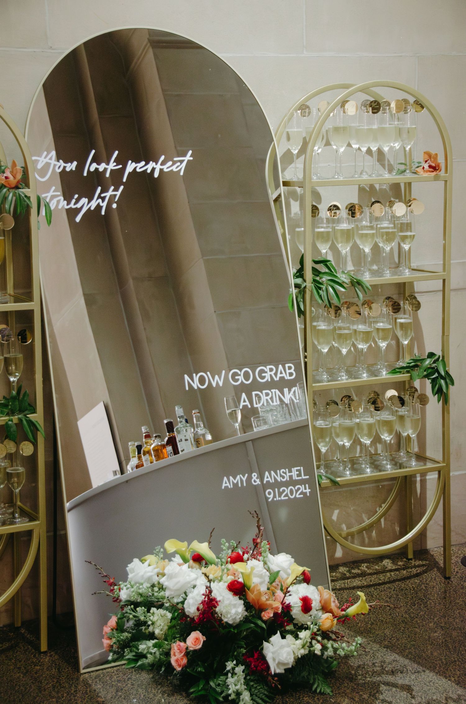Wedding decor display with mirror, neon sign, and champagne shelf arrangement.