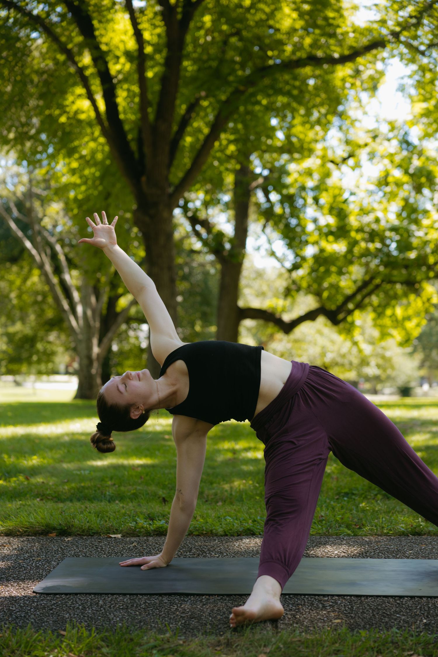A person demonstrates a side plank yoga sequence in a park setting with sunlit trees in the background.
