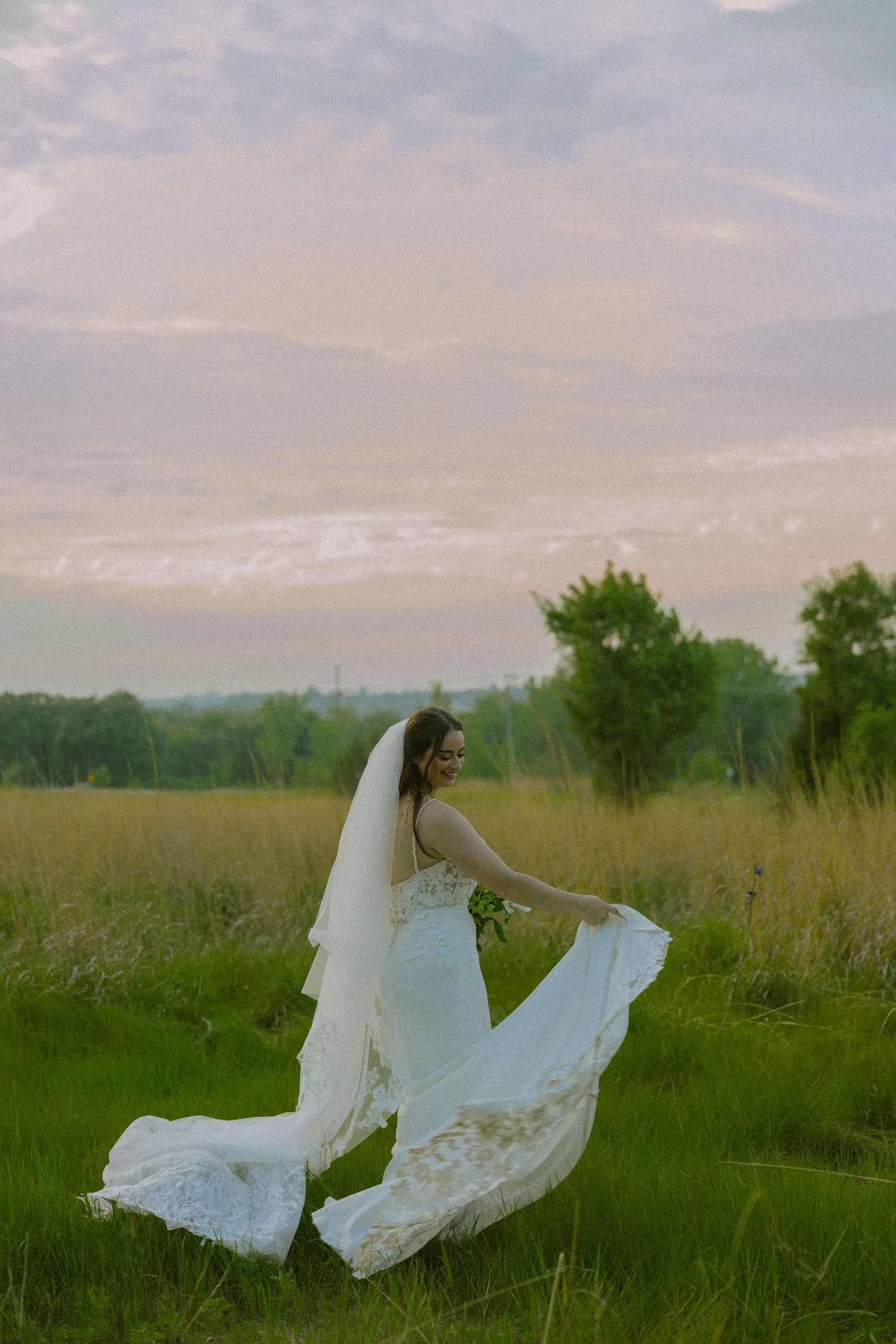 A person in an elegant white wedding dress poses gracefully in a serene meadow at sunset.