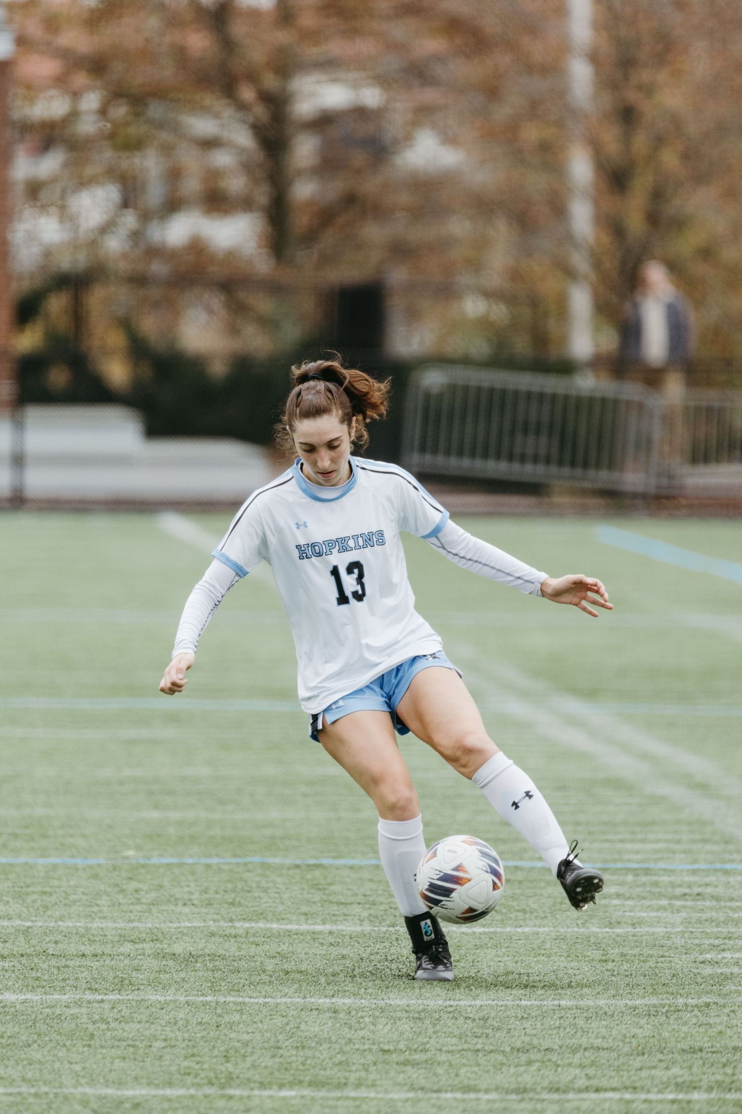 Soccer player in white uniform practices ball control during match on turf field.