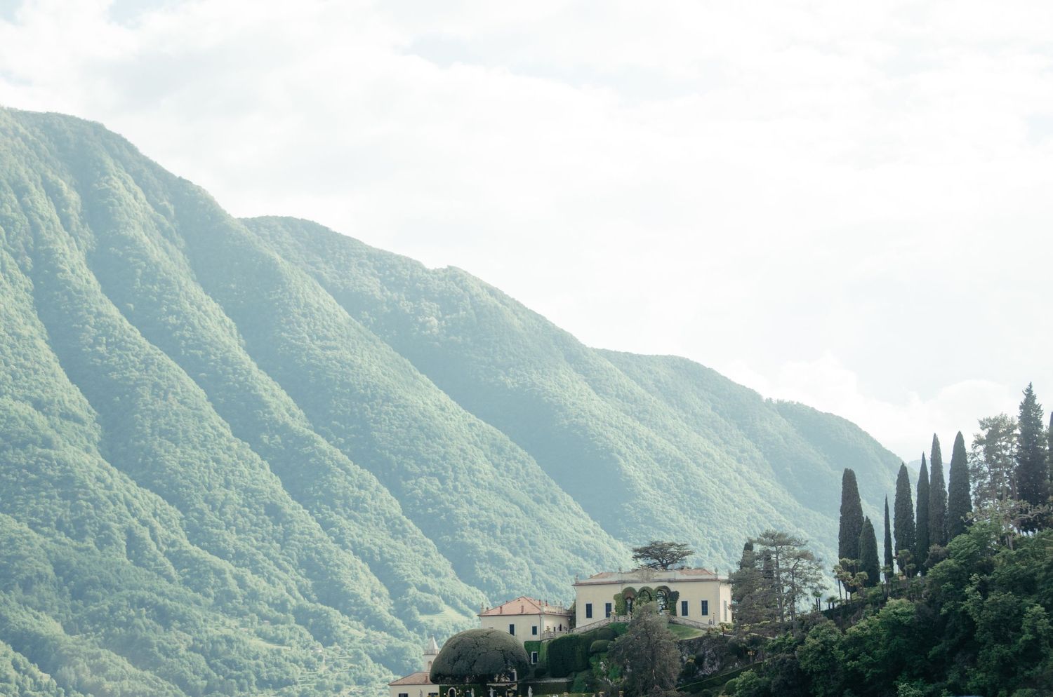 Villa nestled in green mountainside with cypress trees in Mediterranean landscape.