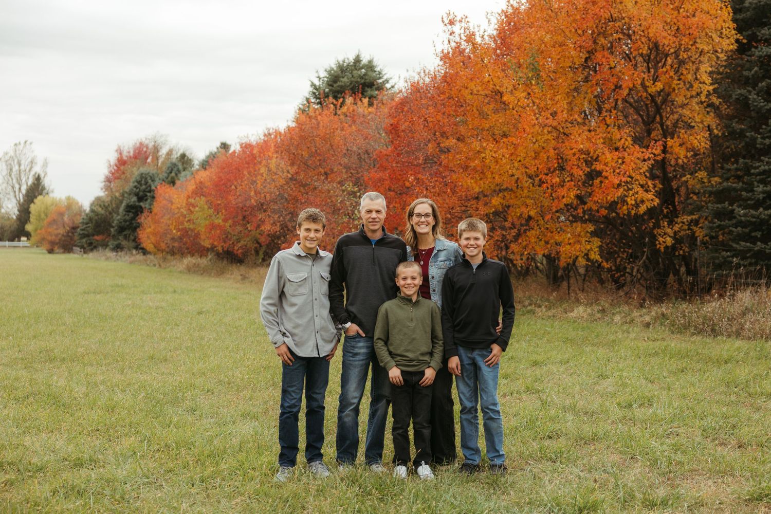 A group stands together in a grassy field with vibrant orange autumn trees in the background during fall.